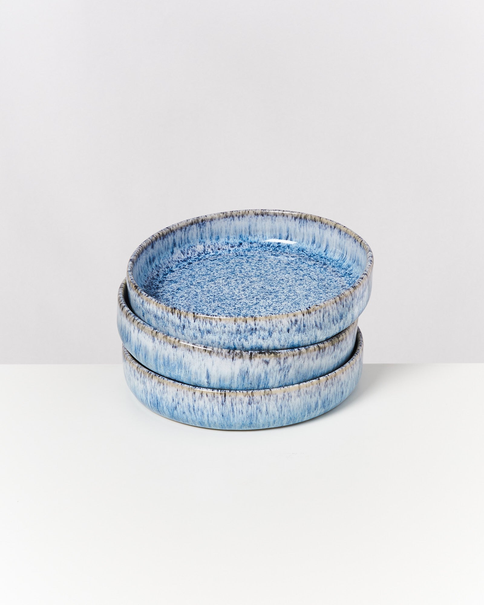 Drei gestapelte, runde Keramikteller in verschiedenen Blautönen auf einer weißen Oberfläche.