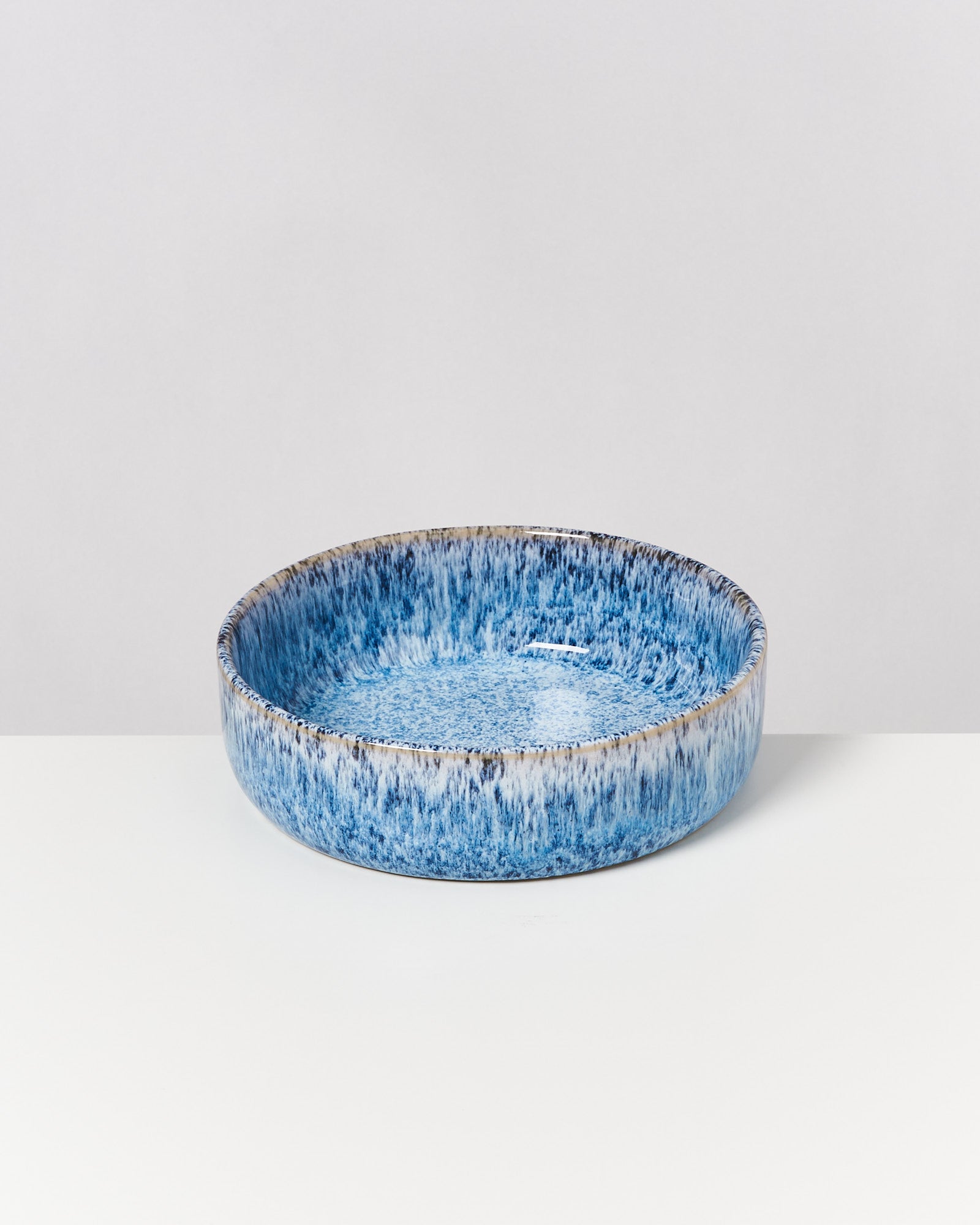 Blaue, runde Keramikschale mit einem kunstvollen, gesprenkelten Muster steht auf einer weißen Oberfläche.