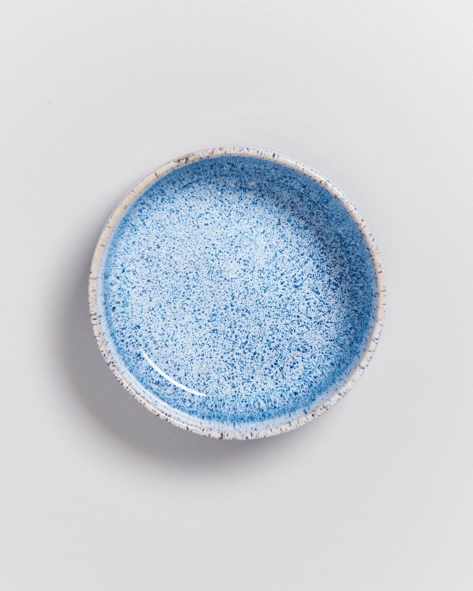 Blauer Keramikteller mit gesprenkeltem Muster auf weißem Hintergrund.