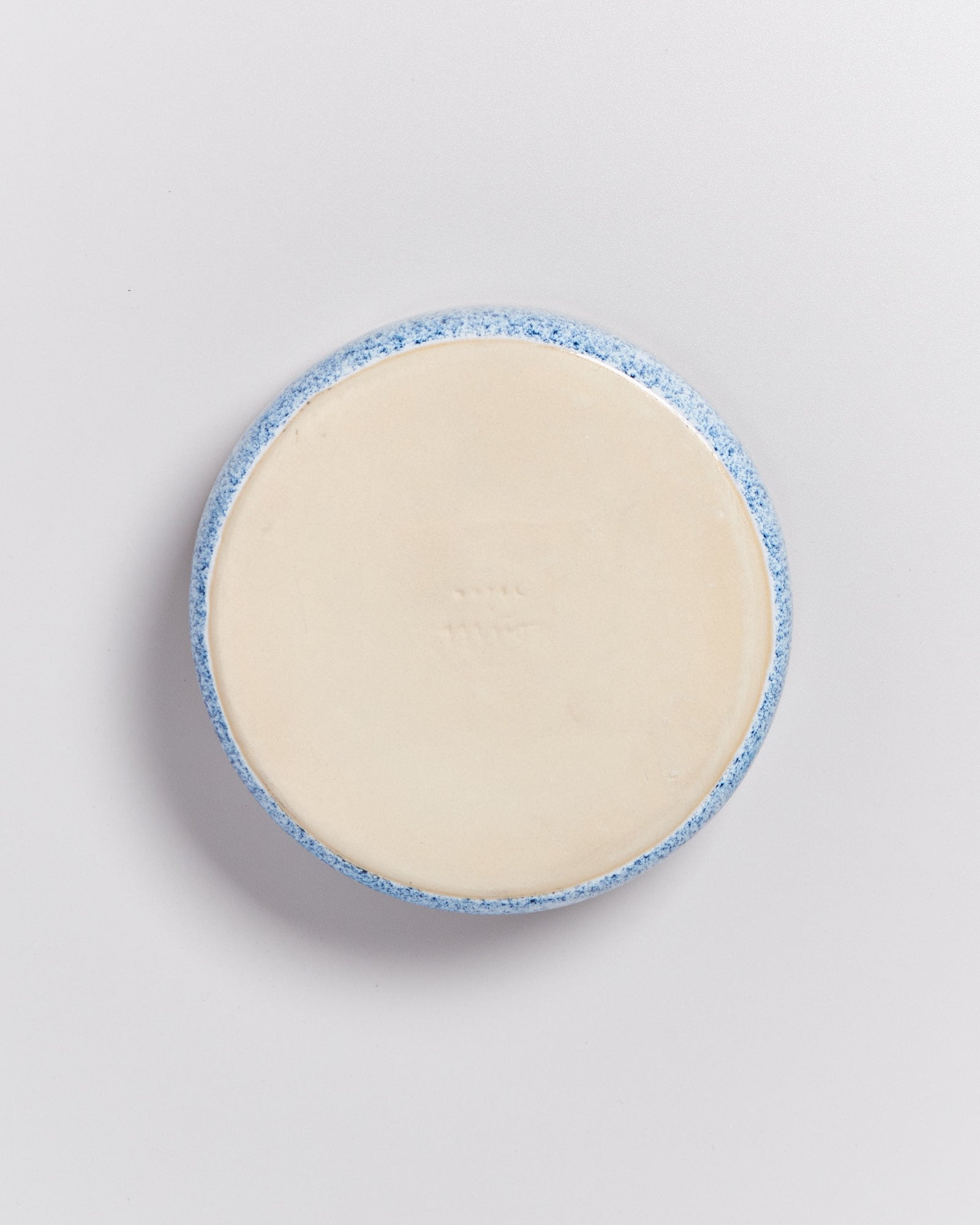 Runde Unterseite einer hellen Keramikschale mit blauem Rand auf weißem Hintergrund.