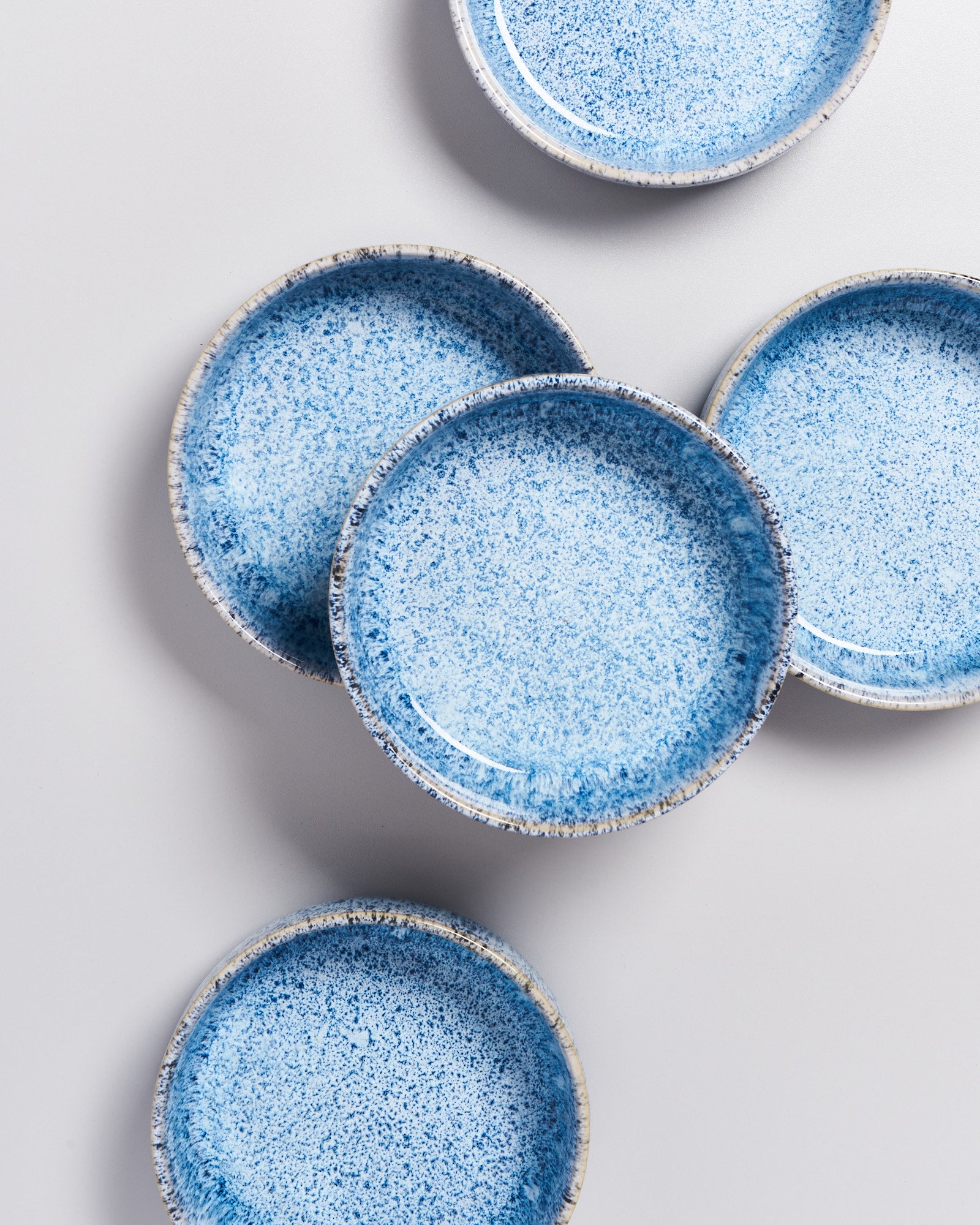 Fünf blaue, gesprenkelte Keramikteller liegen auf einer hellen Oberfläche angeordnet.