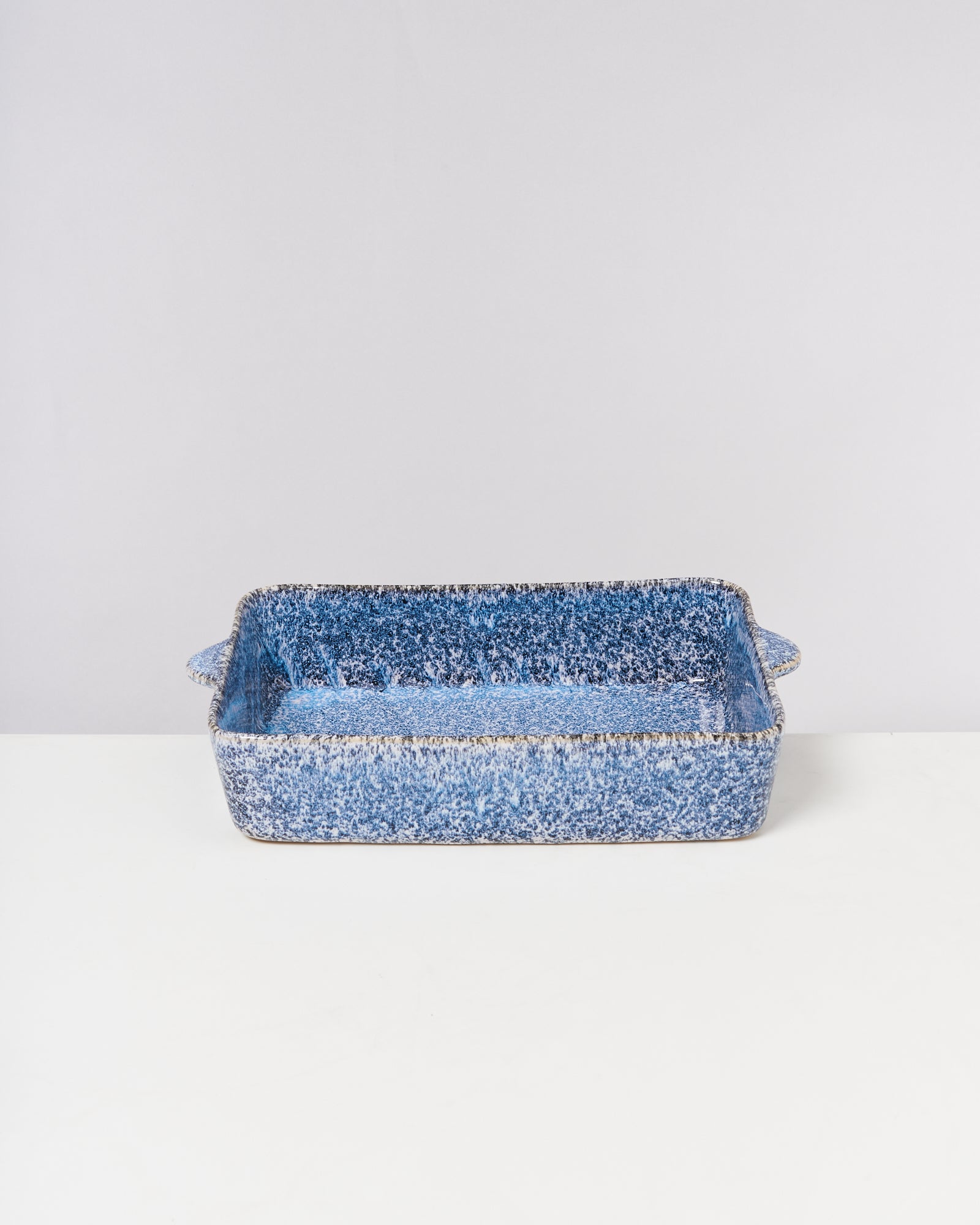 Rechteckige blaue Keramikbackform mit seitlichen Griffen vor grauem Hintergrund.
