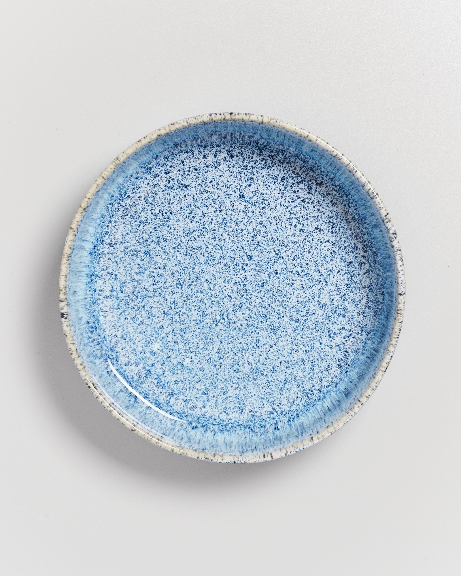 Blauer, gesprenkelter Keramikteller mit breitem Rand auf weißem Hintergrund.