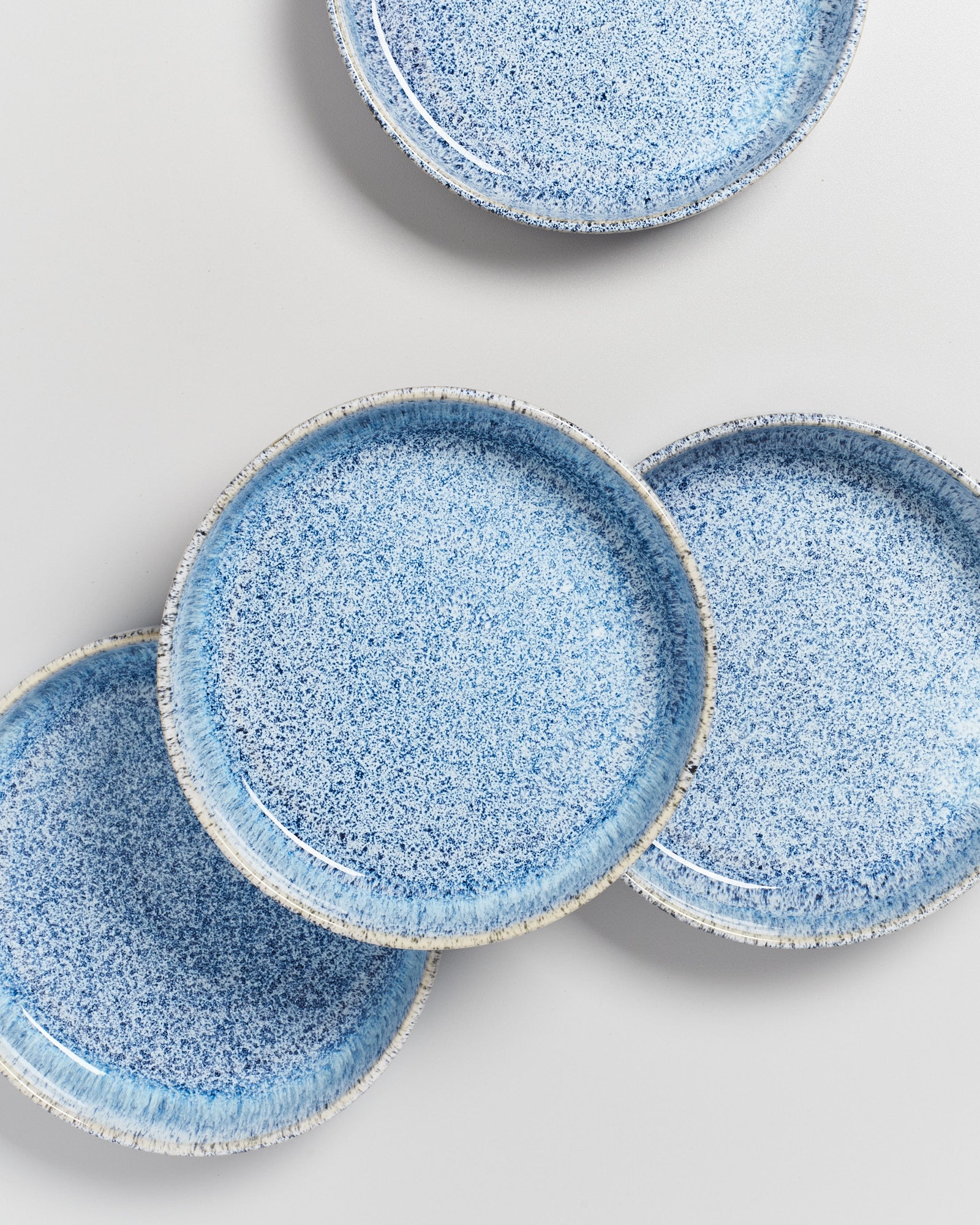 Vier blaue, gesprenkelte Teller liegen teils überlappend auf einer grauen Oberfläche.