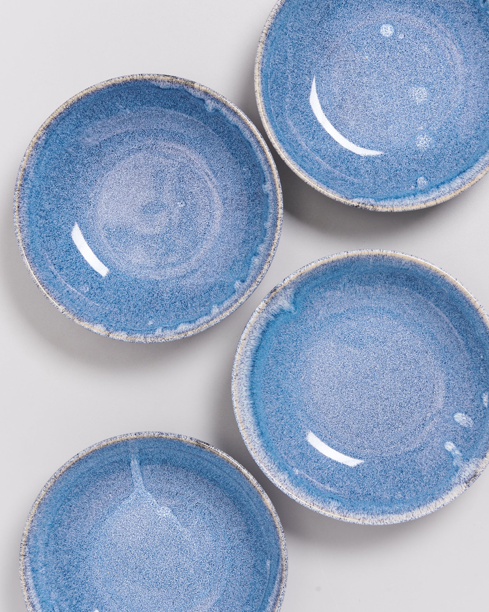 Vier blaue Keramikteller mit gesprenkeltem Muster auf einer hellgrauen Fläche.