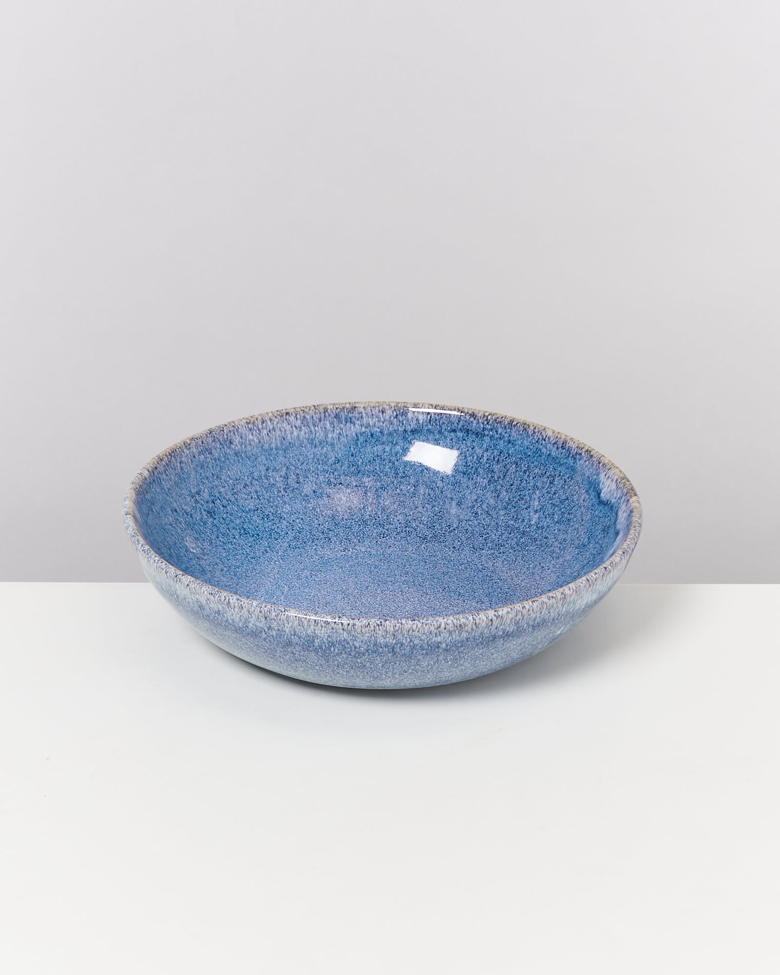 Eine blaue Keramikschale mit gesprenkelter Oberfläche auf einem weißen Untergrund.