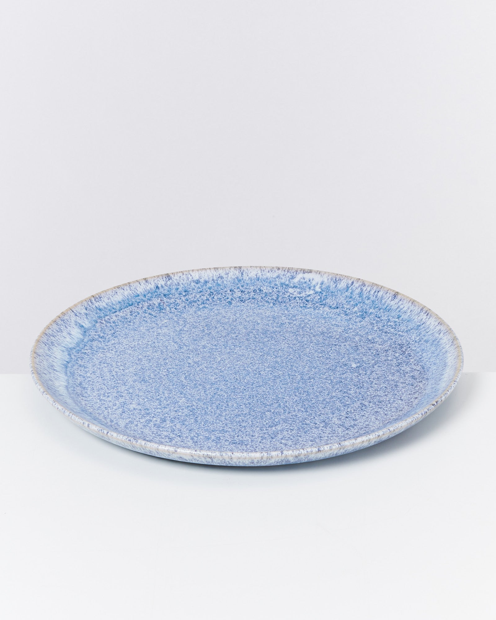 Ein großer, flacher, blau gemusterter Teller auf weißem Hintergrund.