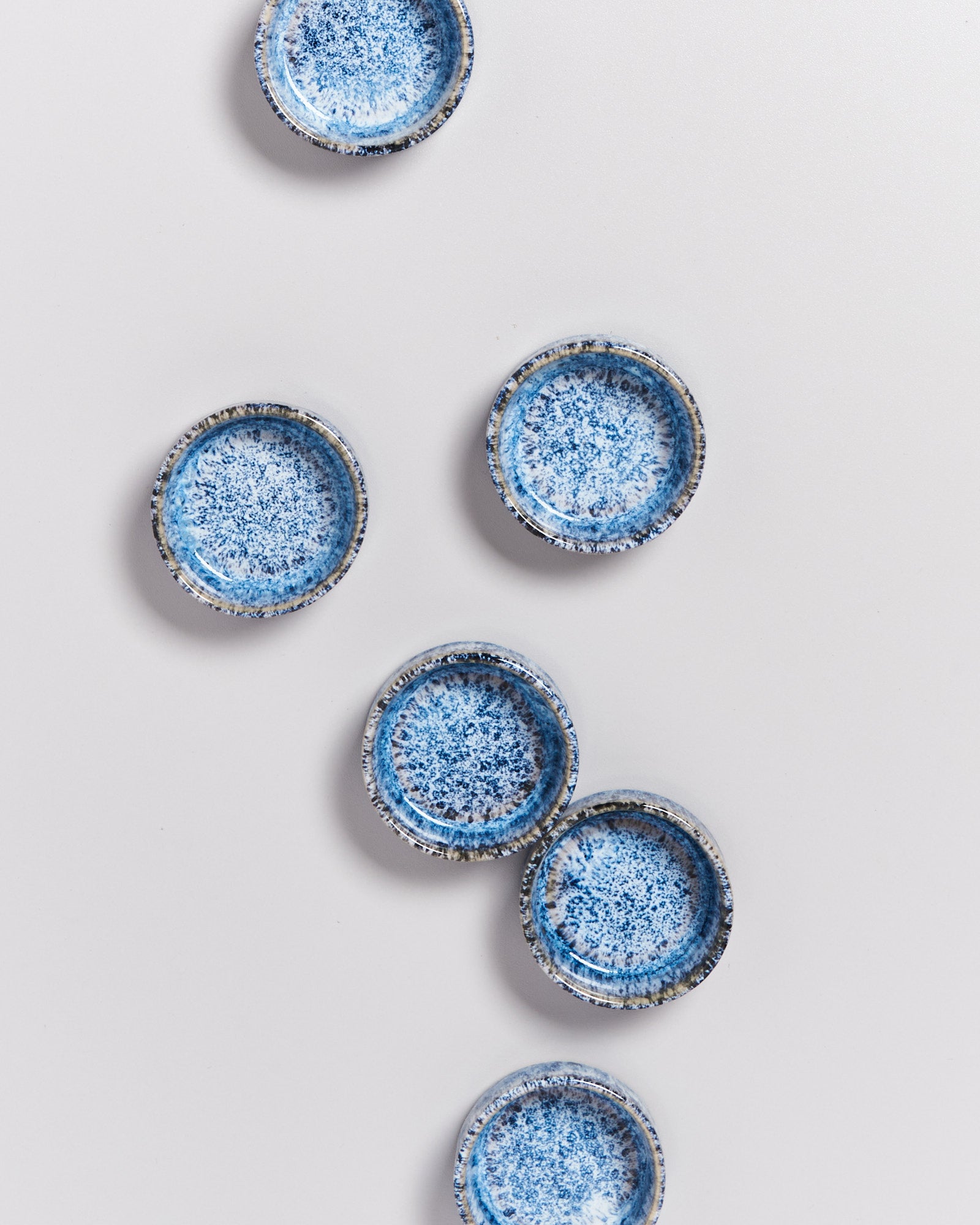 Sechs blau gemusterte Keramikteller liegen auf einem weißen Hintergrund verstreut.