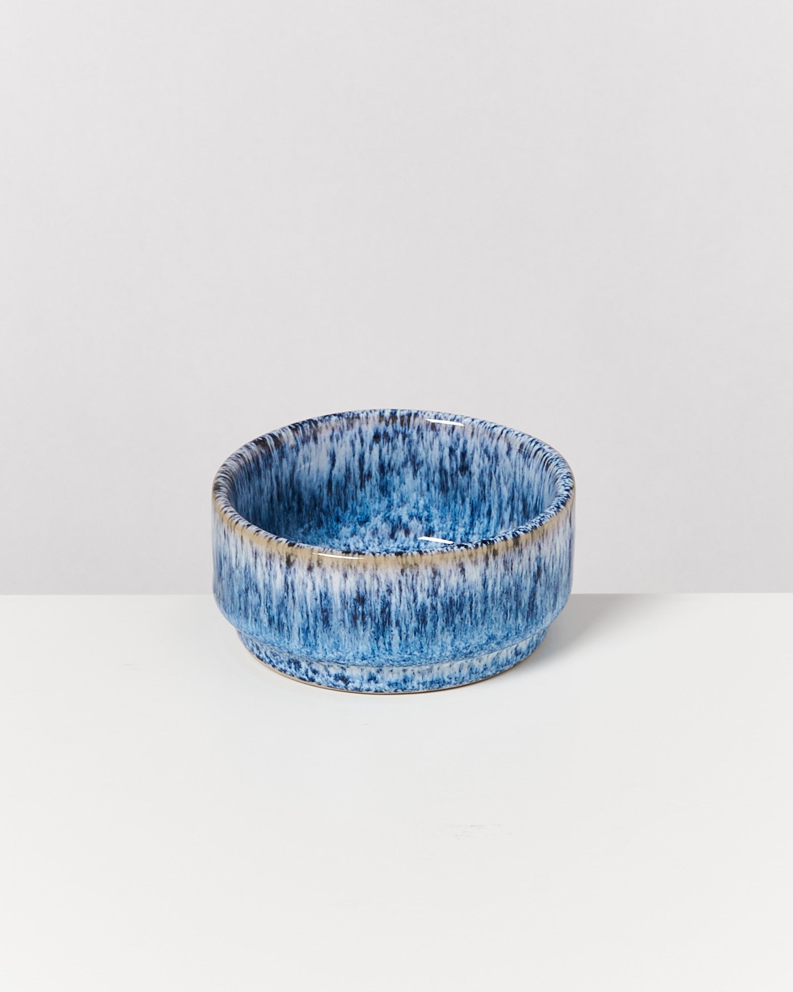 Eine runde blaue Keramikschale mit einem weiß-blauen Muster steht auf einem weißen Tisch vor einem grauen Hintergrund.