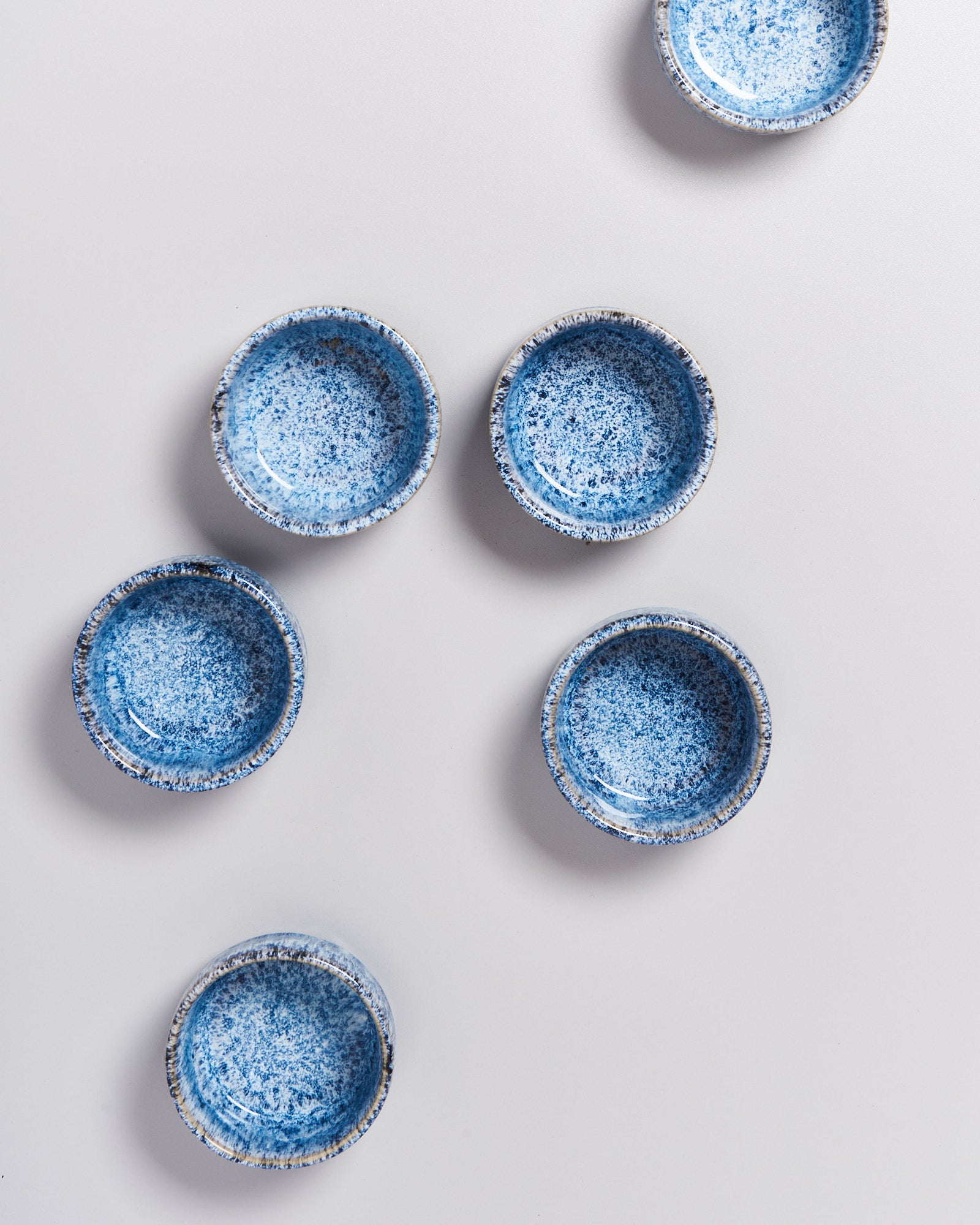 Sechs blaue, gesprenkelte Keramikschalen auf einer weißen Oberfläche arrangiert.