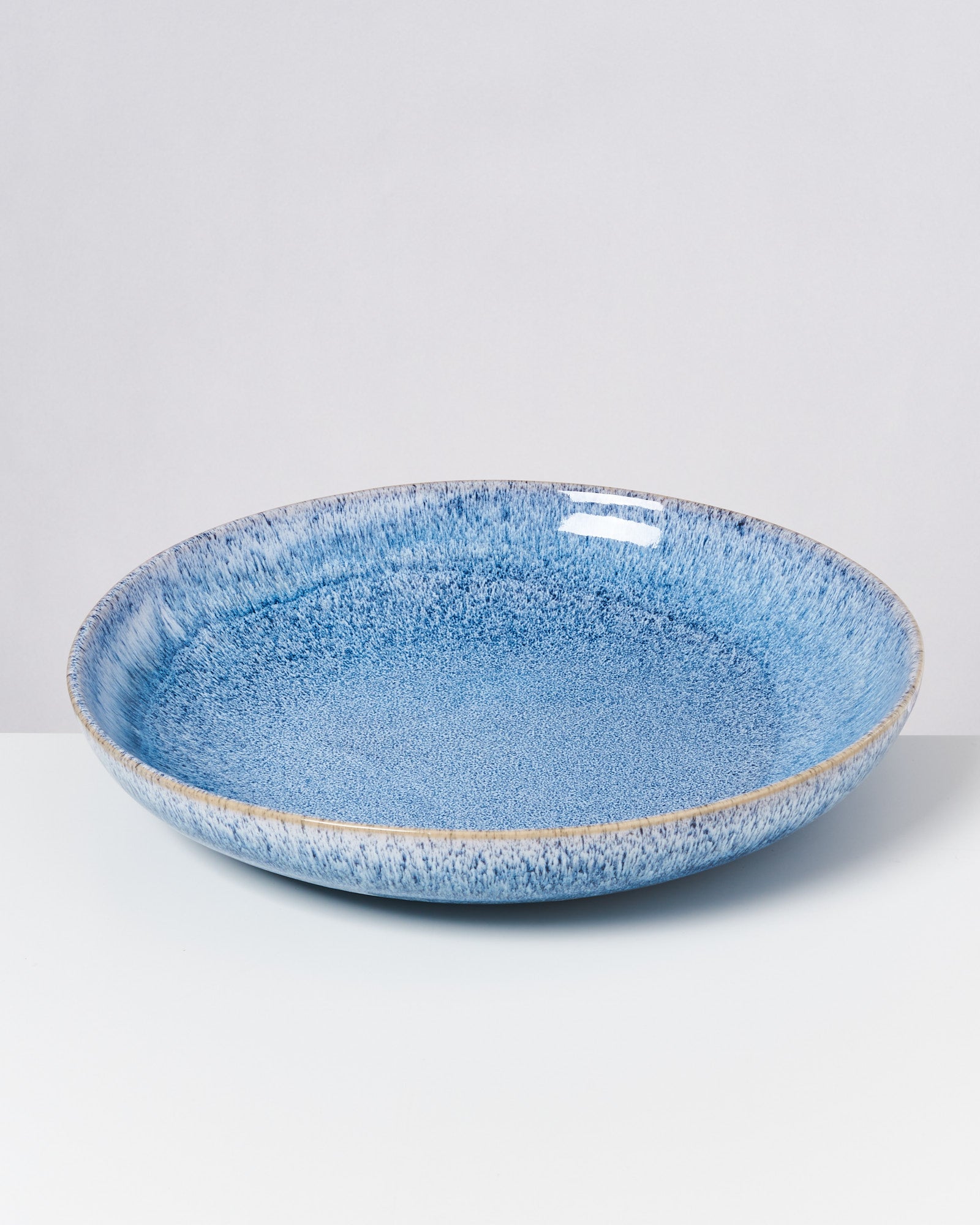 Ein blauer, flacher Keramikteller mit dekorativem Muster auf einem weißen Hintergrund.