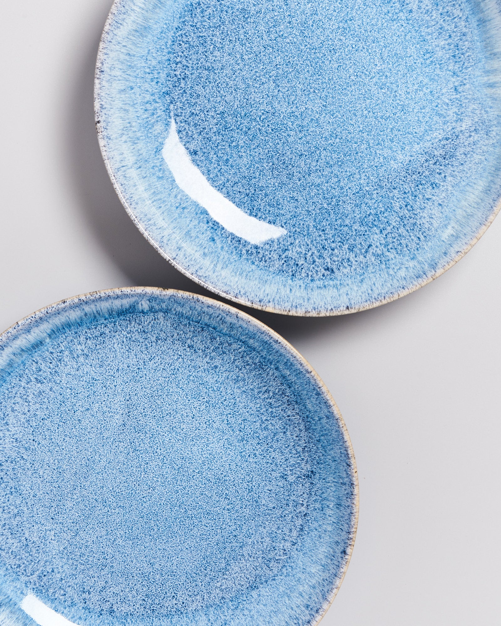 Zwei blaue, strukturierte Teller mit einem feinen Muster liegen auf einem hellgrauen Hintergrund.