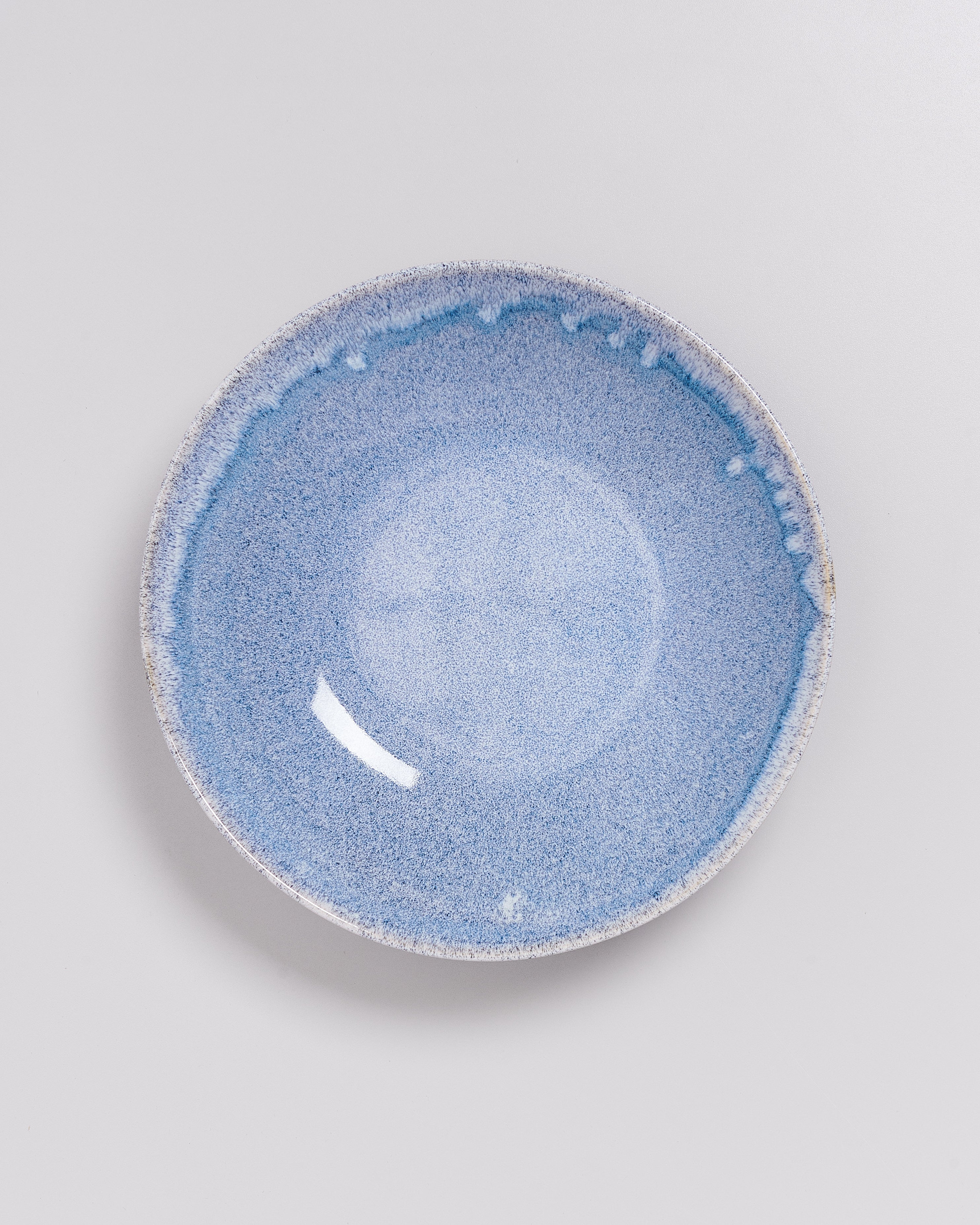 Runder blauer Keramikteller mit gesprenkeltem Design auf weißem Hintergrund.