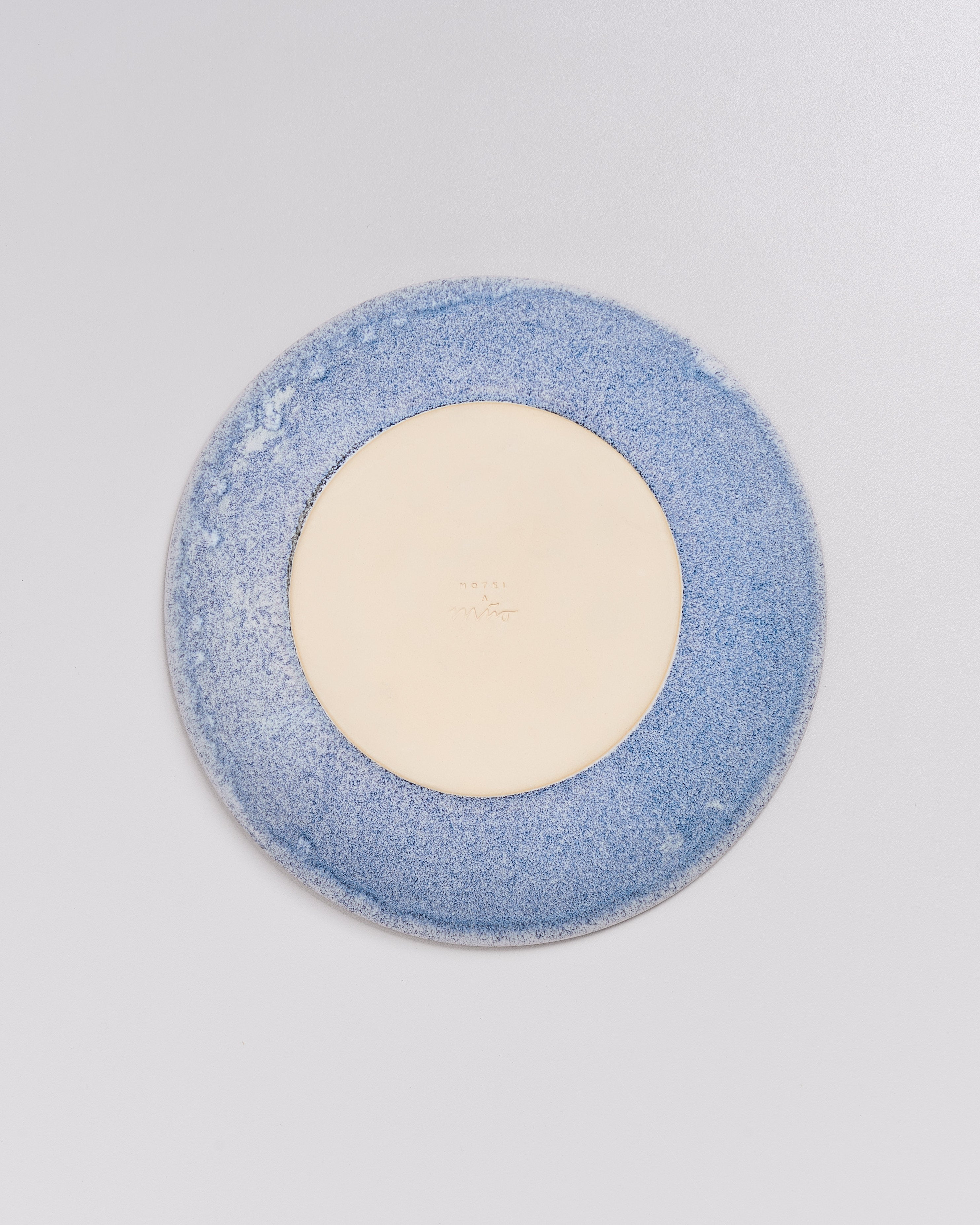 Die Unterseite eines blauen Tellers mit beigem Zentrum auf weißem Hintergrund.