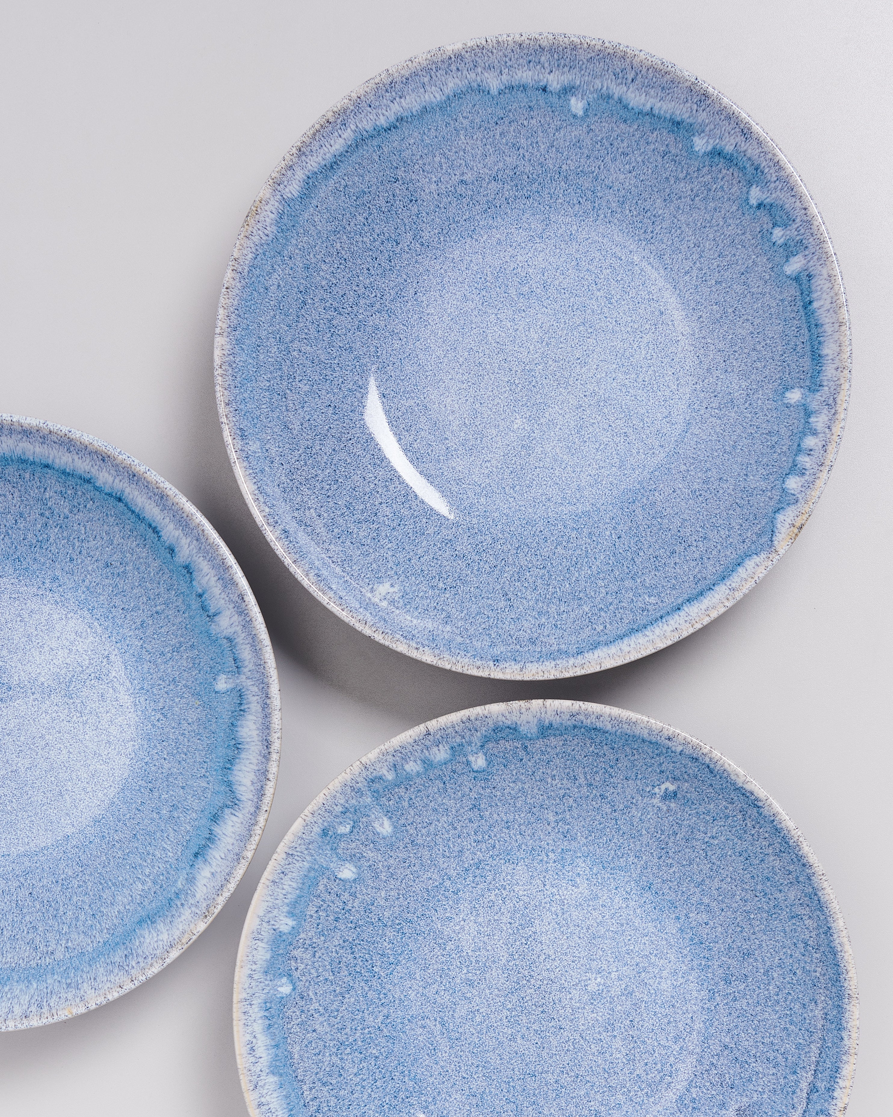 Drei hellblaue Keramikteller mit dunklerem, unregelmäßigem Randmuster auf weißem Hintergrund.