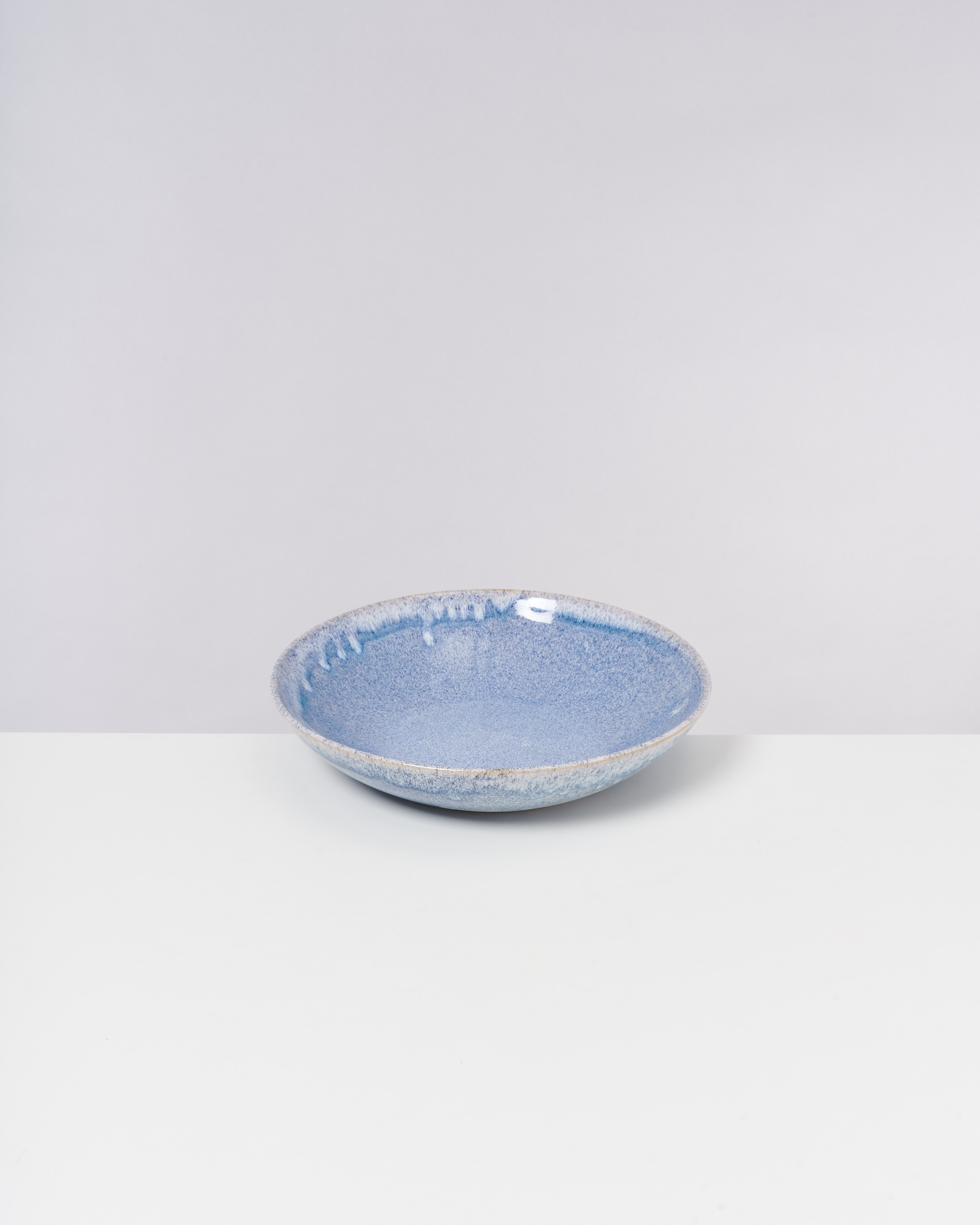 Blaue Keramikschüssel mit mattierter Oberfläche auf einer weißen Oberfläche vor grauem Hintergrund.