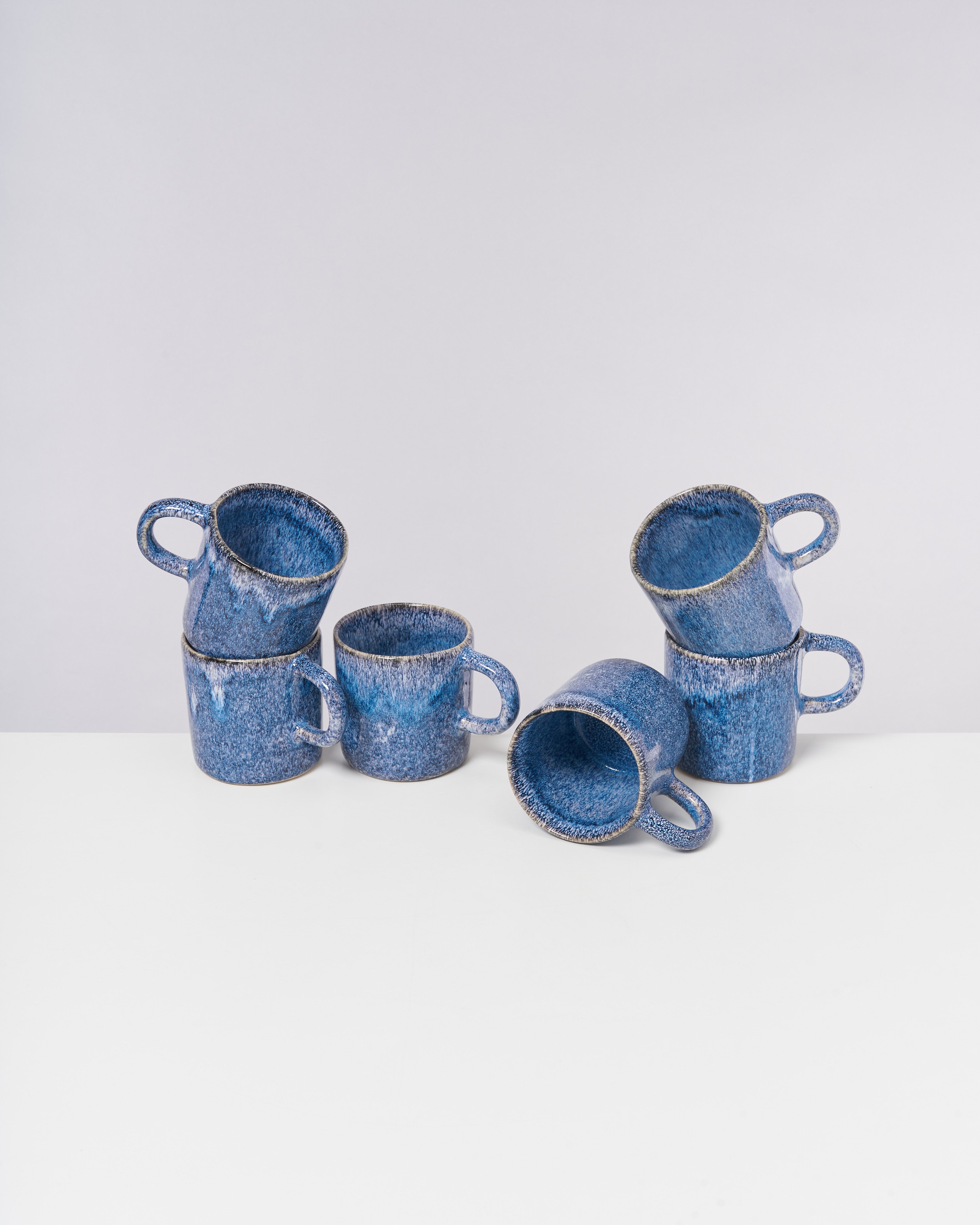 Sechs blaue Keramiktassen in verschiedenen Positionen auf einer weißen Oberfläche.