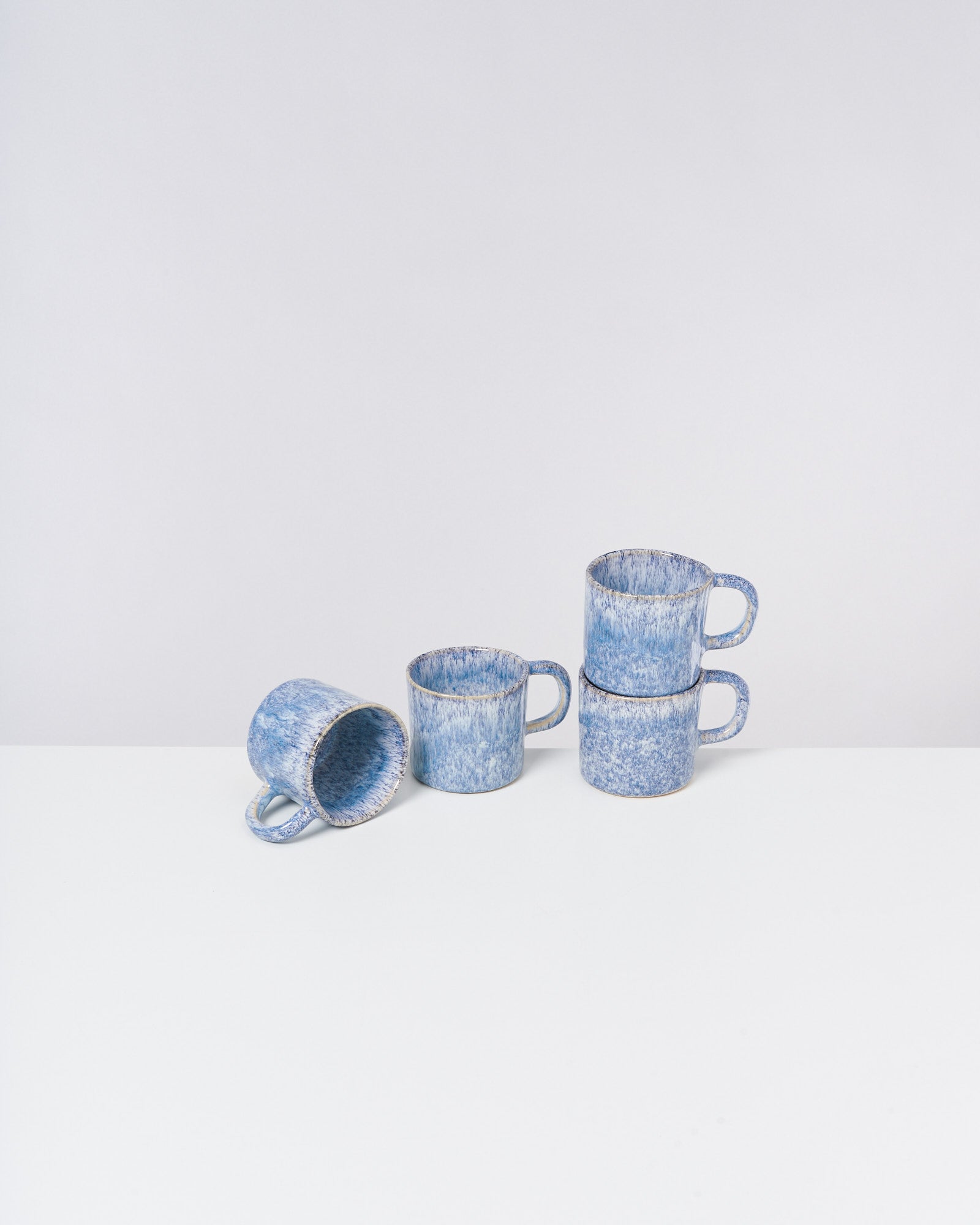 Drei blaue Keramiktassen, zwei gestapelt, eine liegt auf der Seite auf einem weißen Hintergrund.