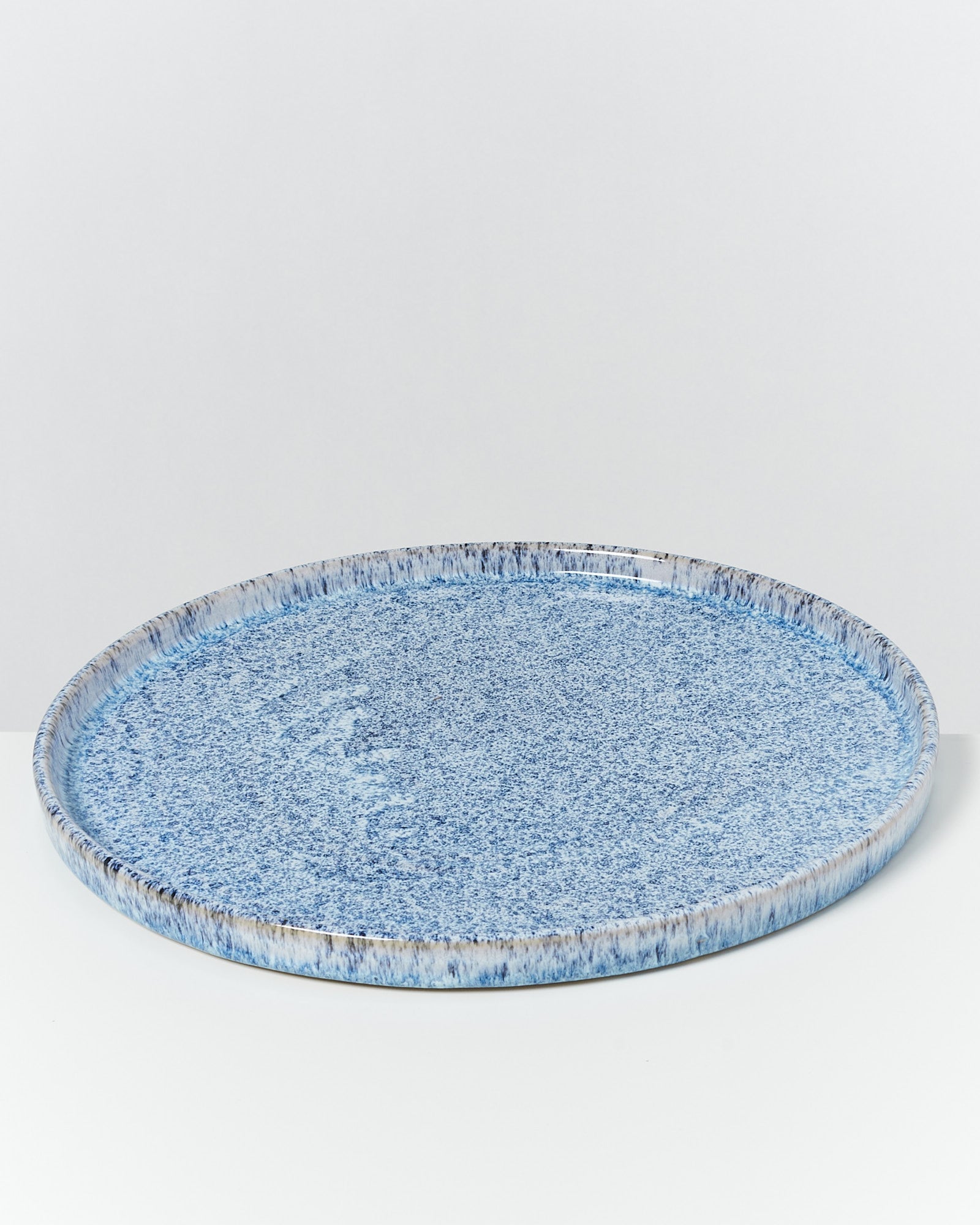 Runde, blau gesprenkelte Keramikplatte auf weißem Hintergrund.