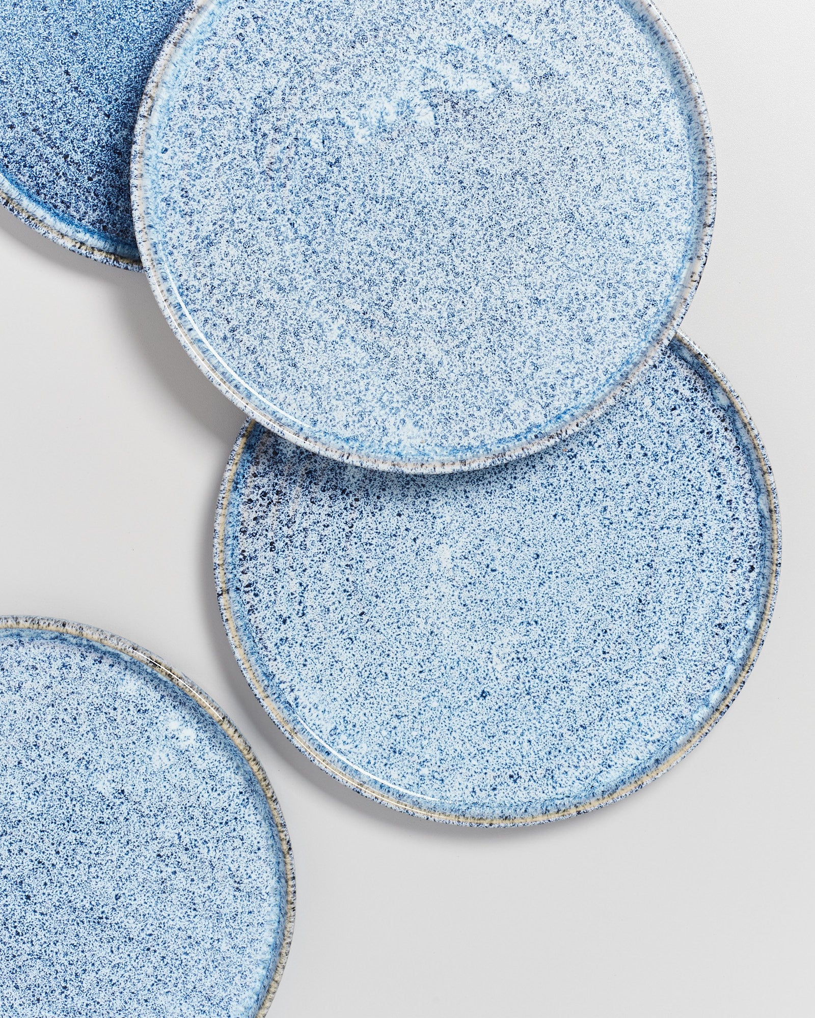 Drei blaue, gesprenkelte Teller auf einem weißen Hintergrund, leicht überlappend angeordnet.