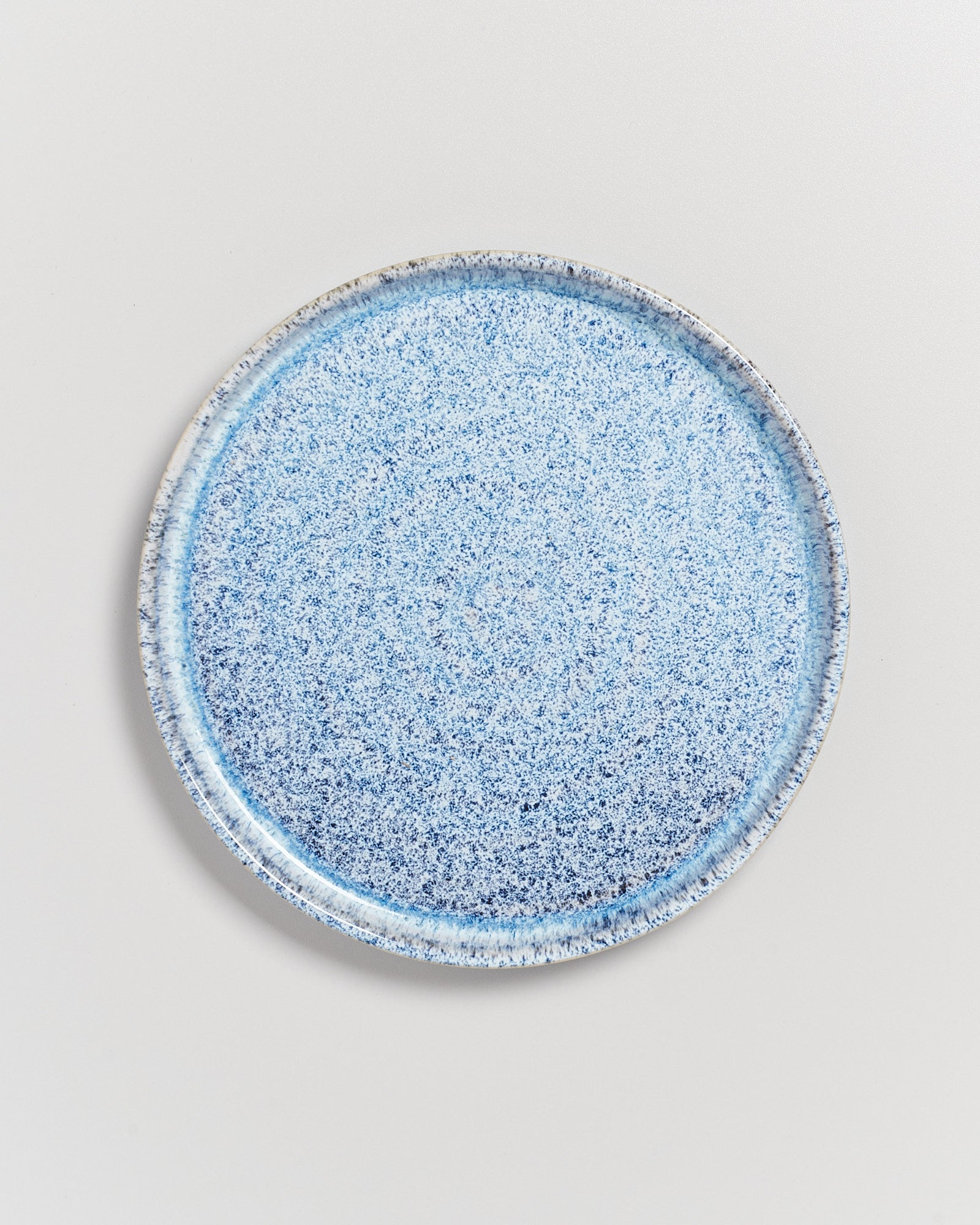Blauer Keramikteller mit gesprenkeltem Muster auf weißem Hintergrund.