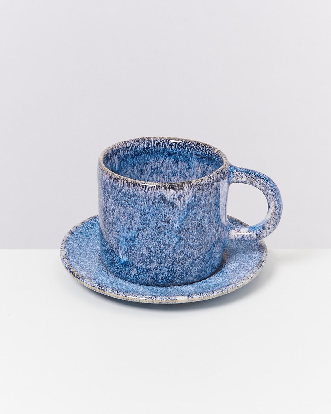 Blaue Keramiktasse mit Untertasse auf weißem Hintergrund.