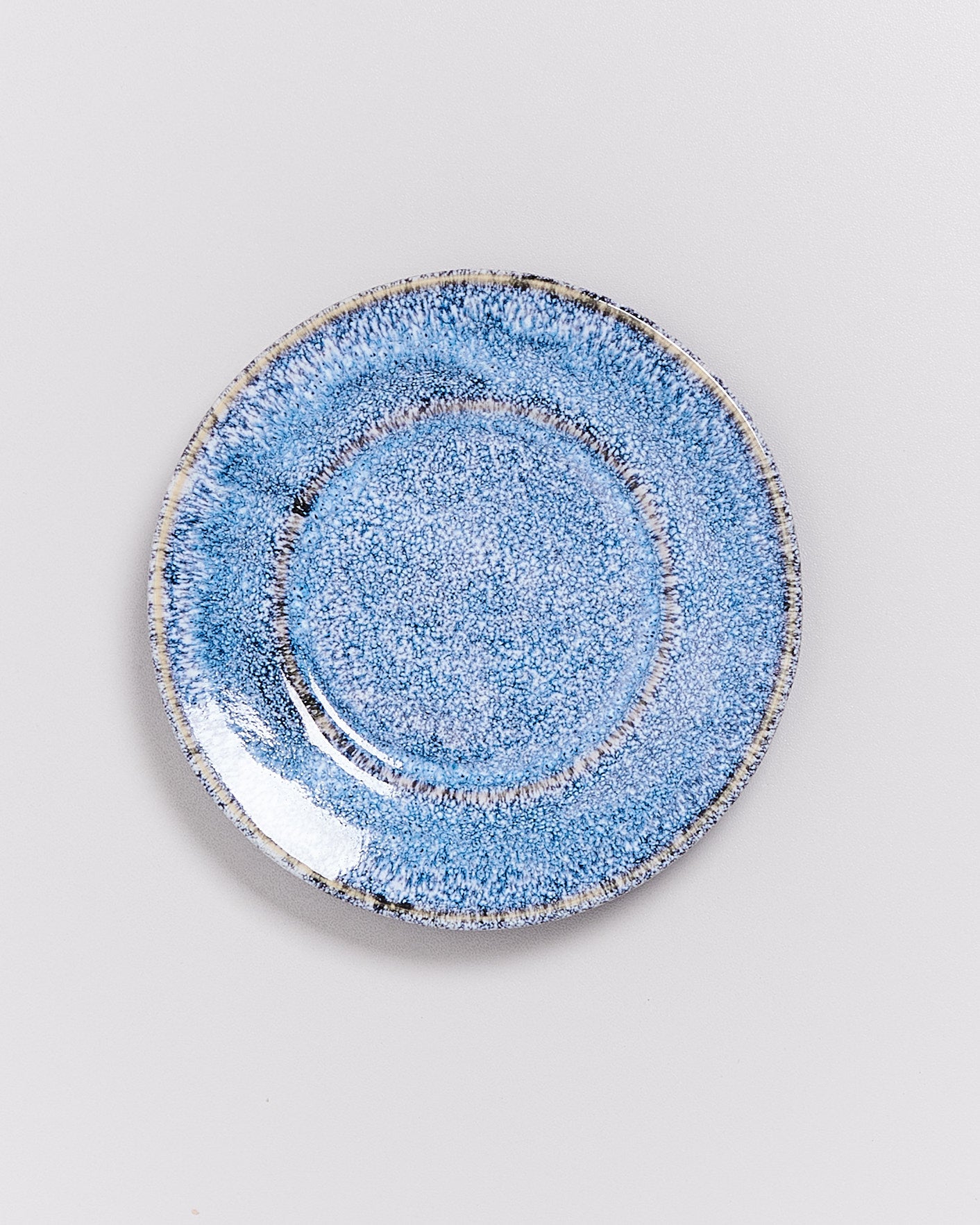 Ein weiß-blauer Keramikteller mit gesprenkeltem Muster liegt auf einem weißen Hintergrund.