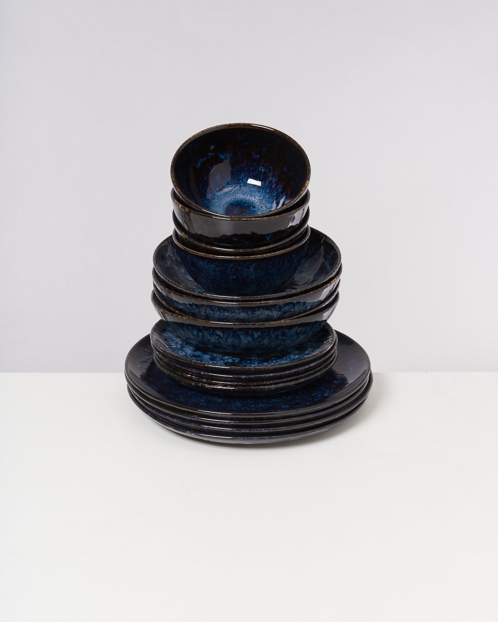 Ein Stapel aus blauen Keramiktellern und -schalen steht auf einem weißen Tisch vor neutralem Hintergrund.