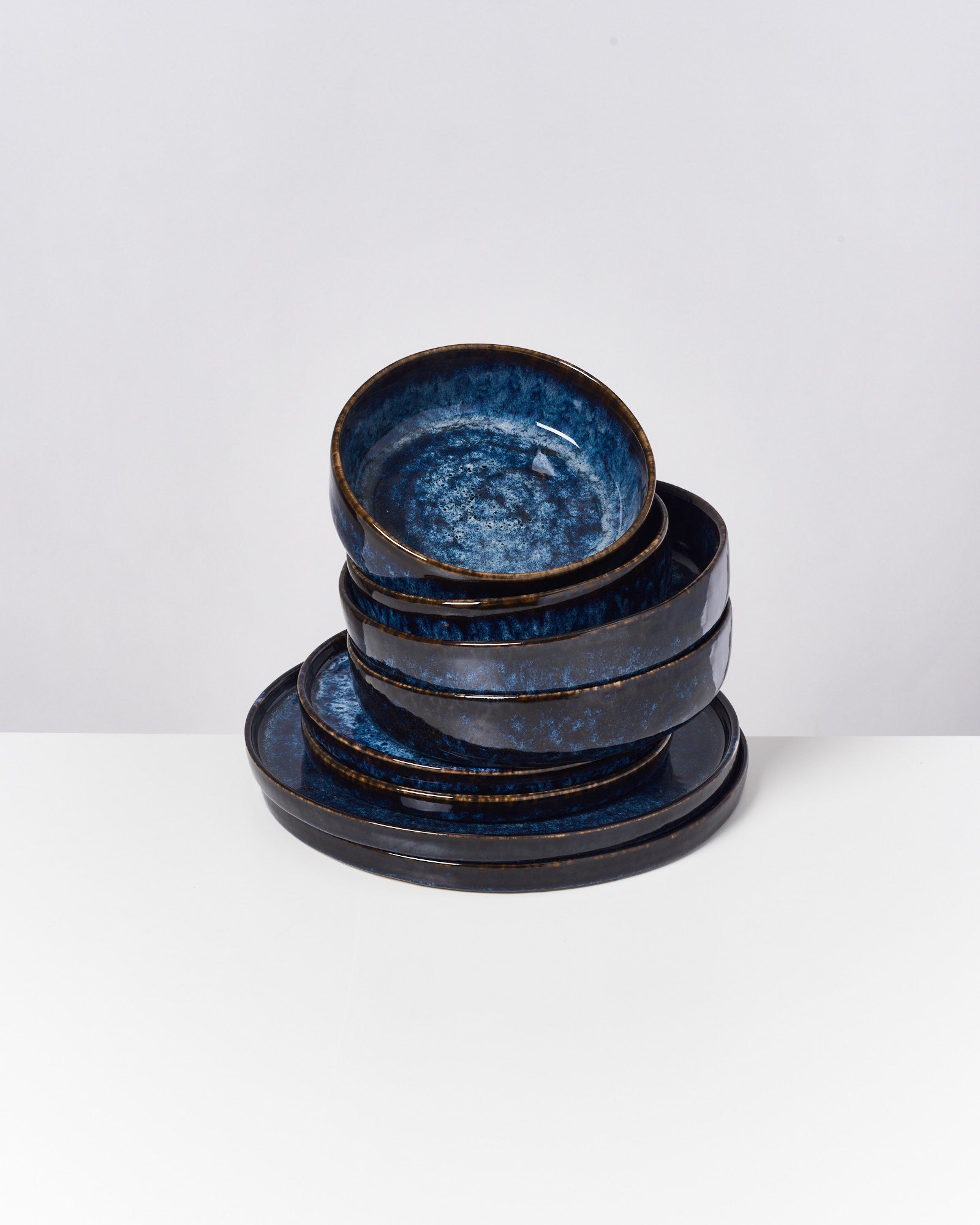 Ein Stapel von dunklen, blau-schwarzen Keramiktellern auf einem weißen Hintergrund.