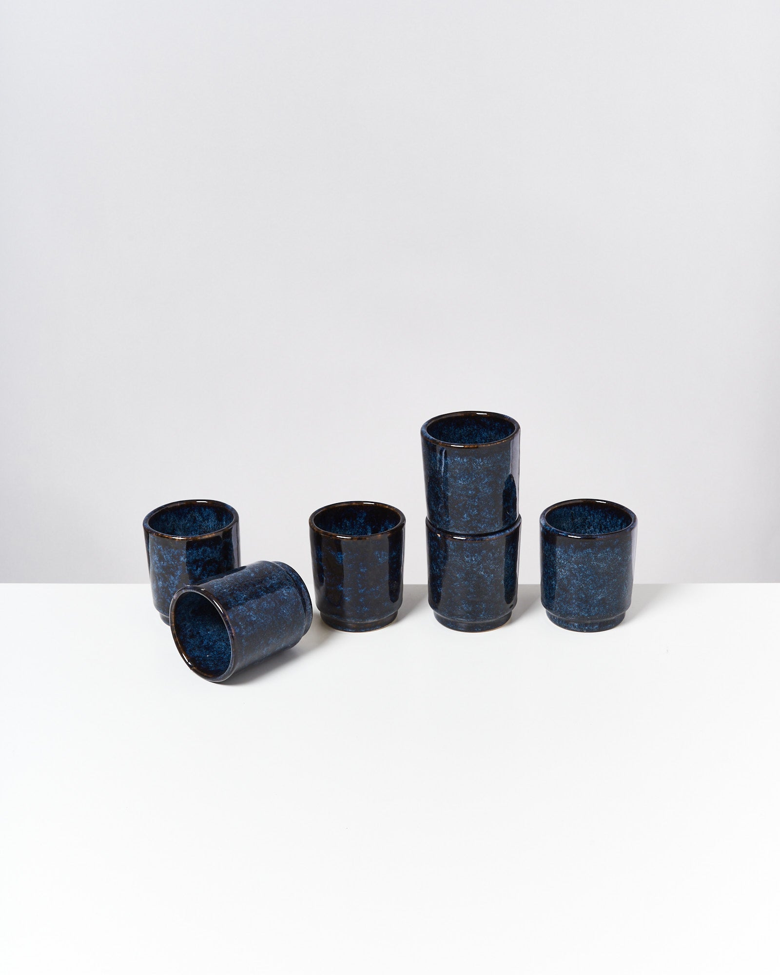 Sieben blaue Becher mit marmorierter Oberfläche stehen auf einem weißen Tisch, einer ist umgekippt.