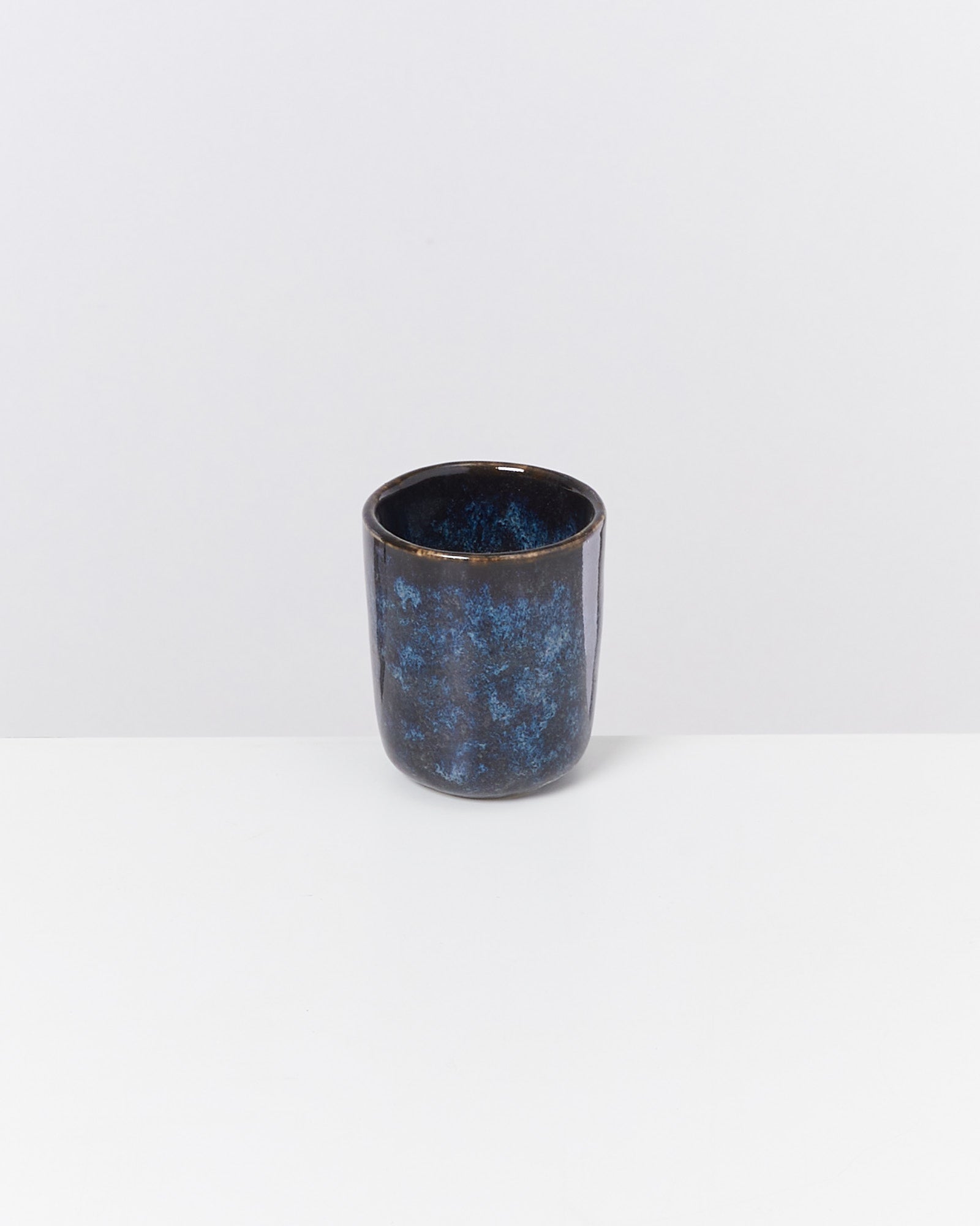 Blauer, keramikartiger Becher auf weißem Hintergrund fotografiert.