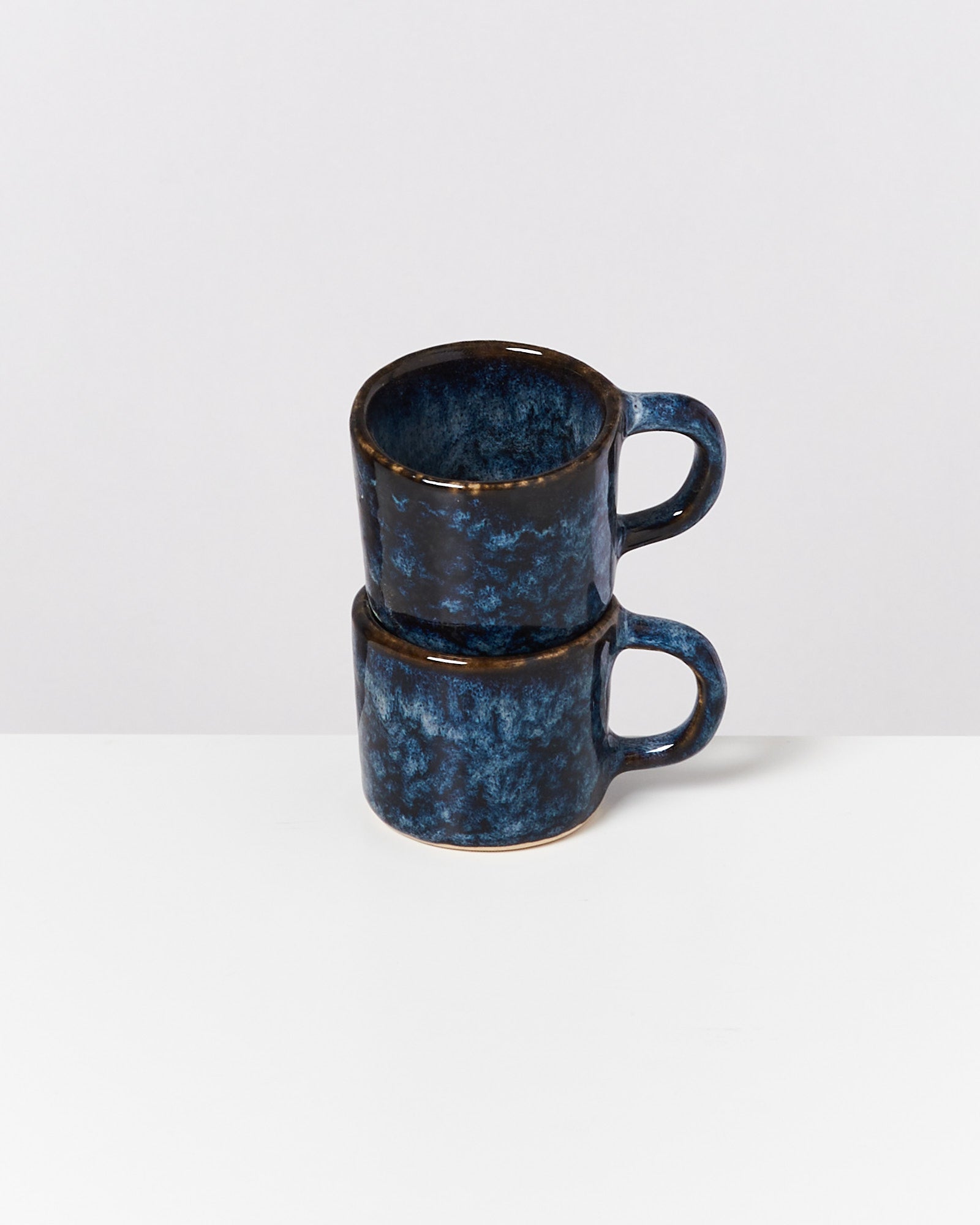 Zwei gestapelte blaue Keramiktassen mit marmoriertem Muster auf weißem Hintergrund.