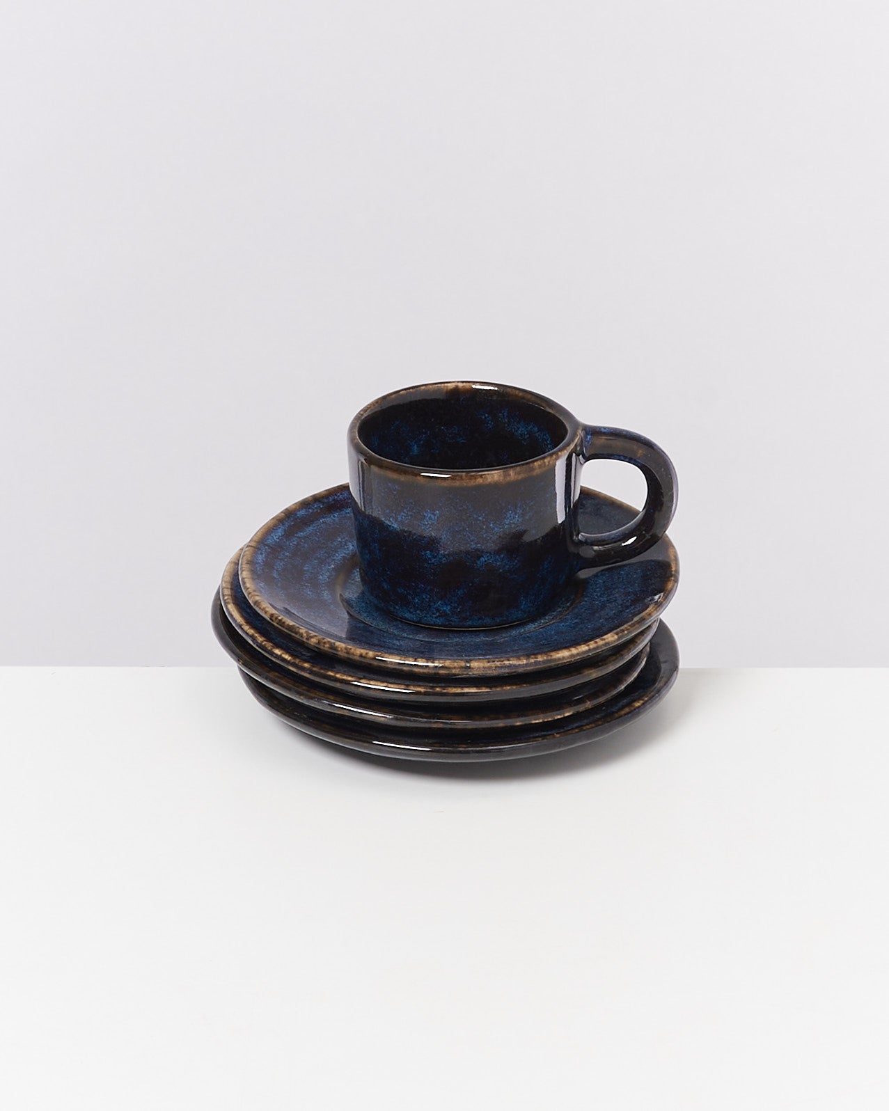 Dunkelblaue Tasse mit Untertasse auf gestapelten Tellern, vor neutralem Hintergrund.