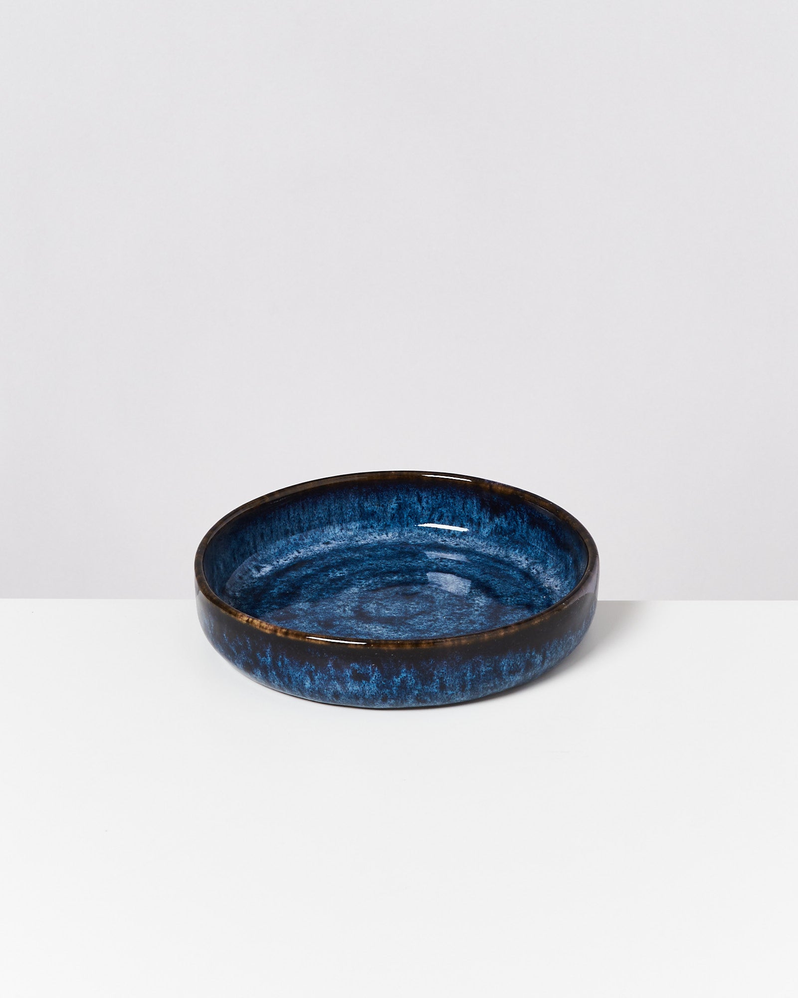 Runde, blaue Keramikschale mit dunklen Rändern auf weißem Hintergrund.