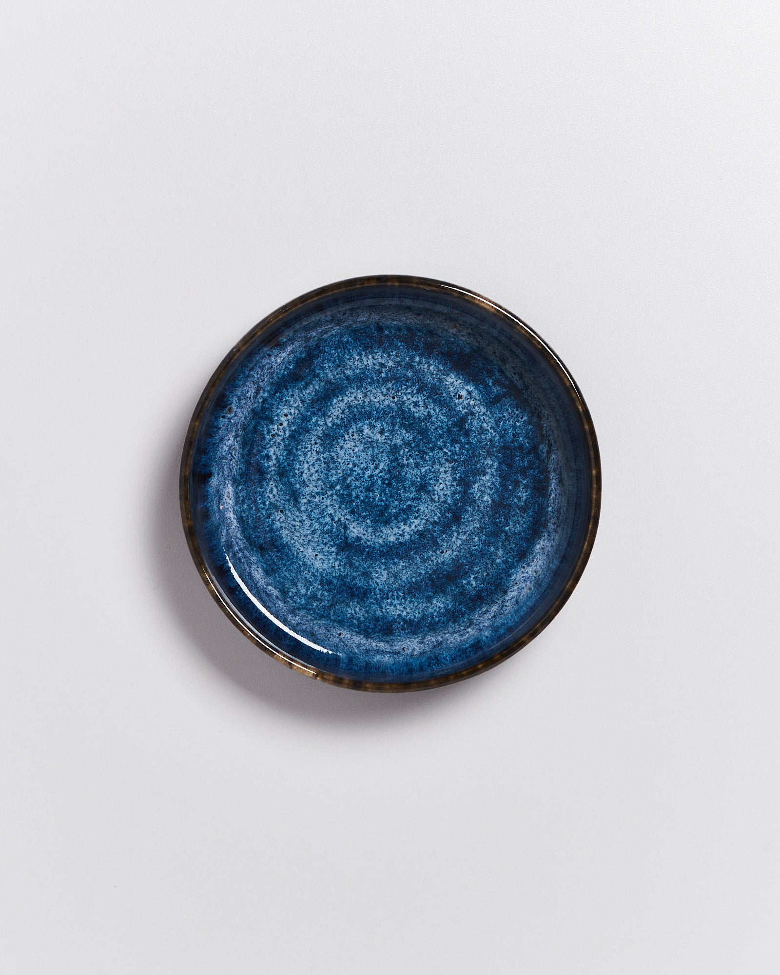 Dunkelblauer Keramikteller mit konzentrischem Muster auf weißem Hintergrund.