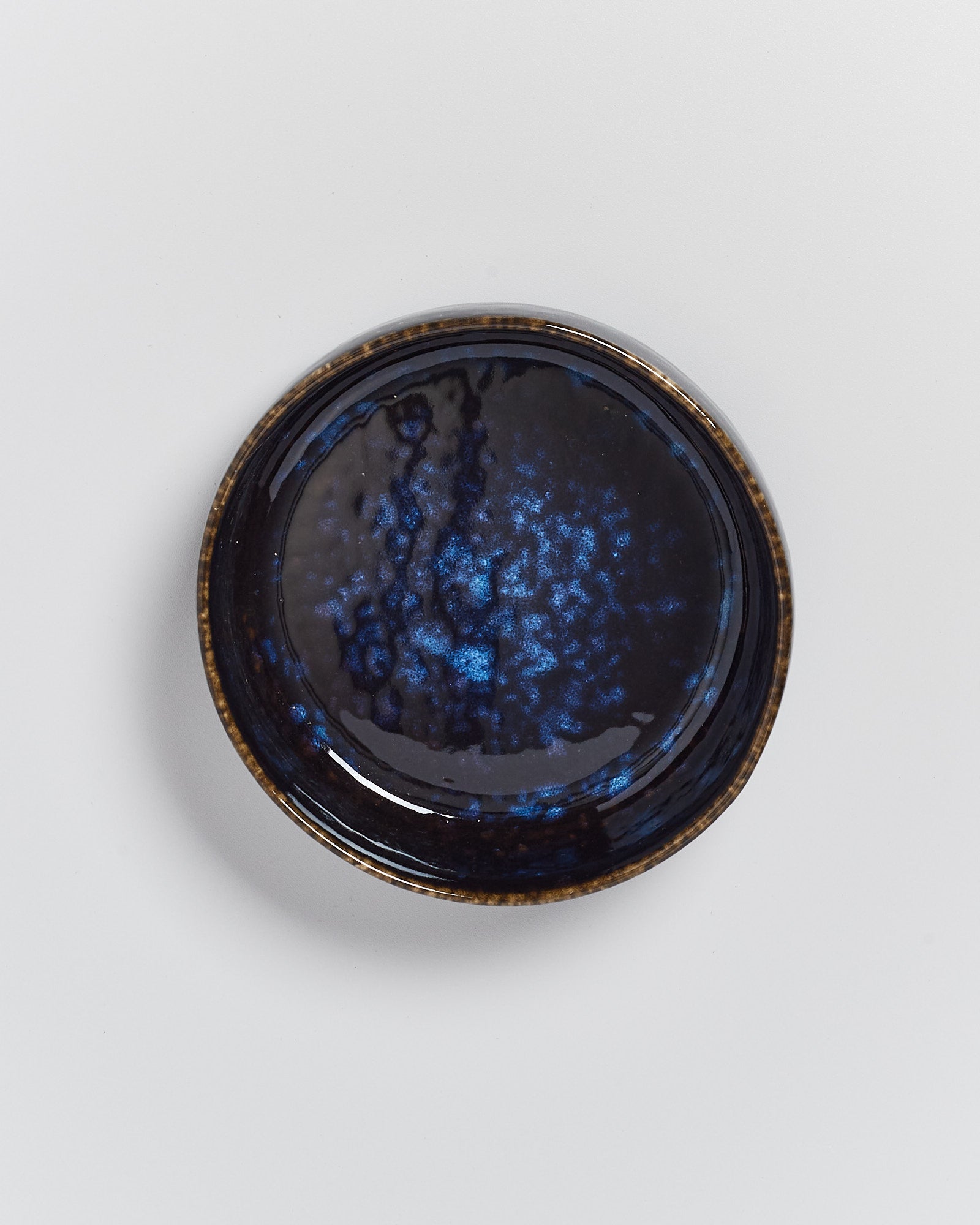 Dunkelblauer, runder Keramikteller mit marmorierter Oberfläche auf weißem Hintergrund.