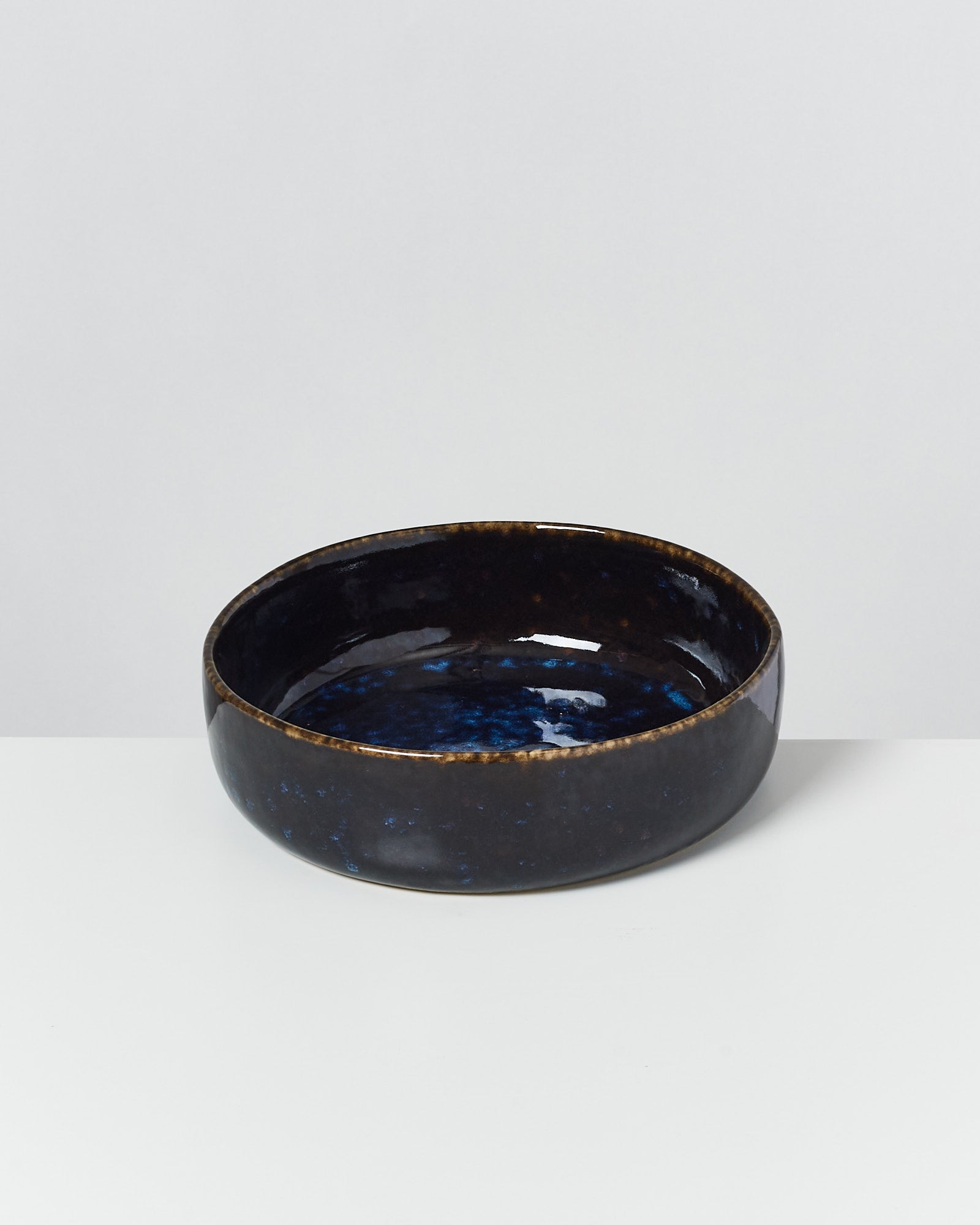 Schwarze Keramikschale mit blauer Glasurinnenseite, auf weißem Hintergrund.