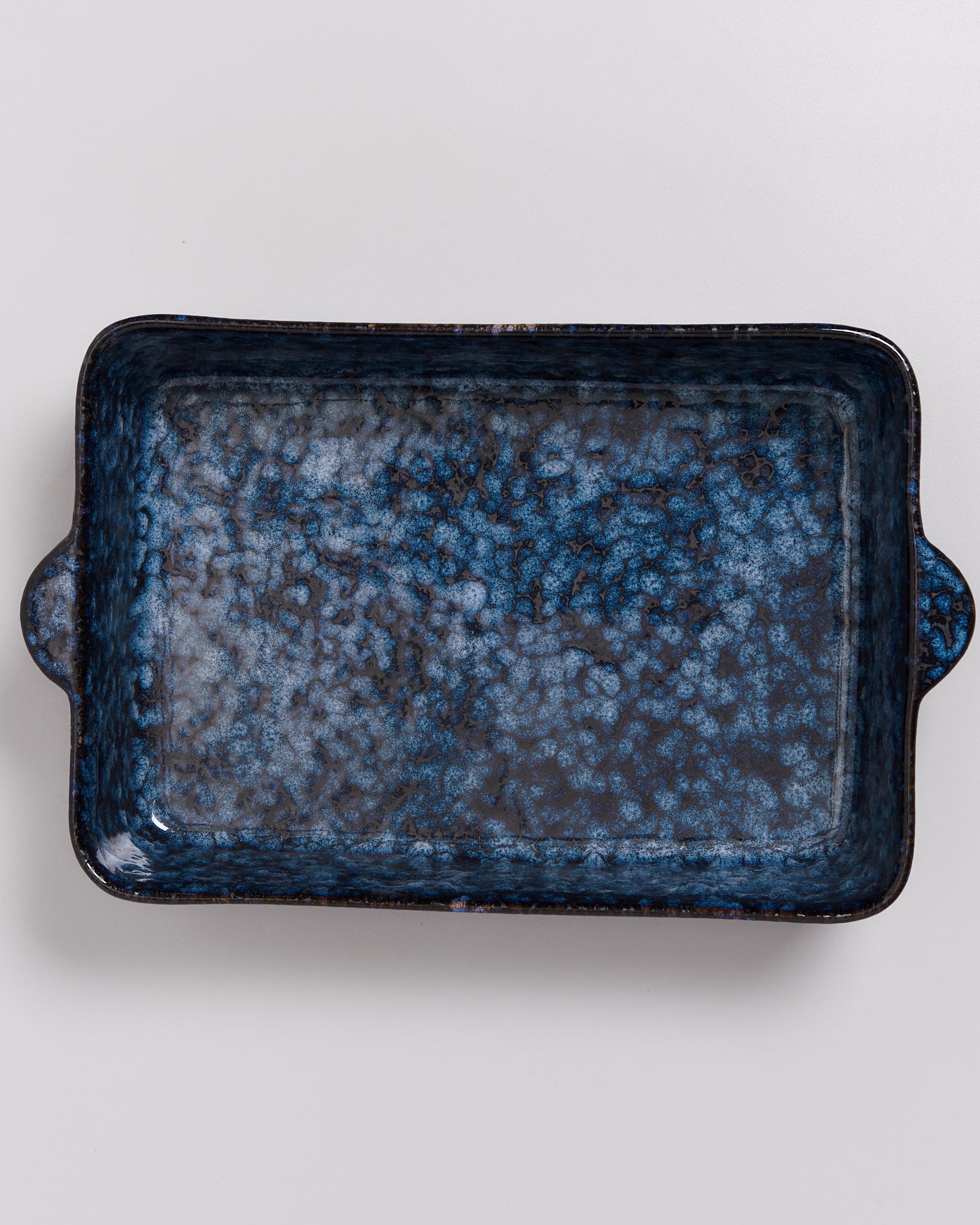 Rechteckige, blaue Keramikform mit speckigem Muster und kleinen Griffen auf einem hellen Hintergrund.