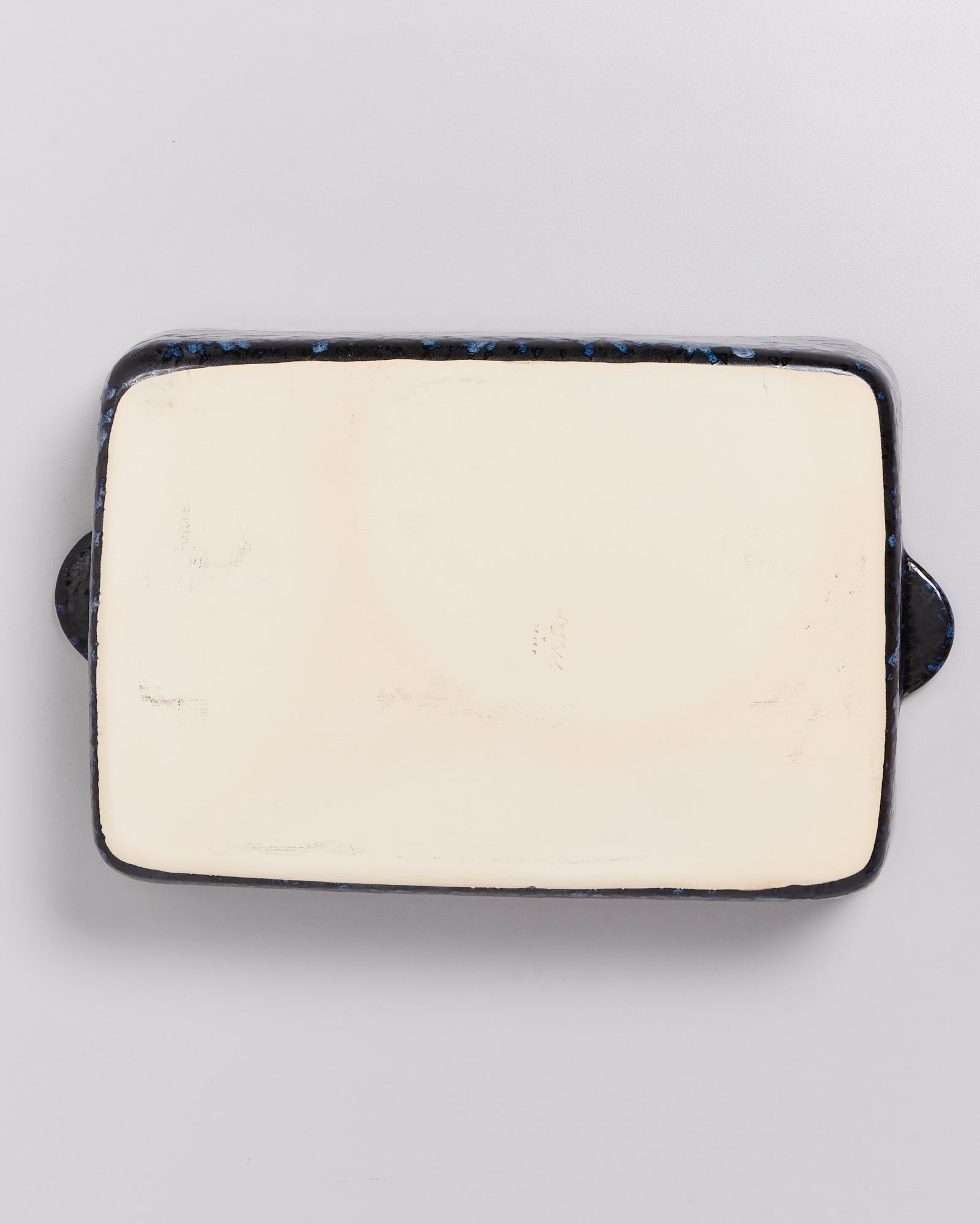 Rechteckige, beige Keramikplatte mit schwarzem Rand und Griffen auf hellem Hintergrund.