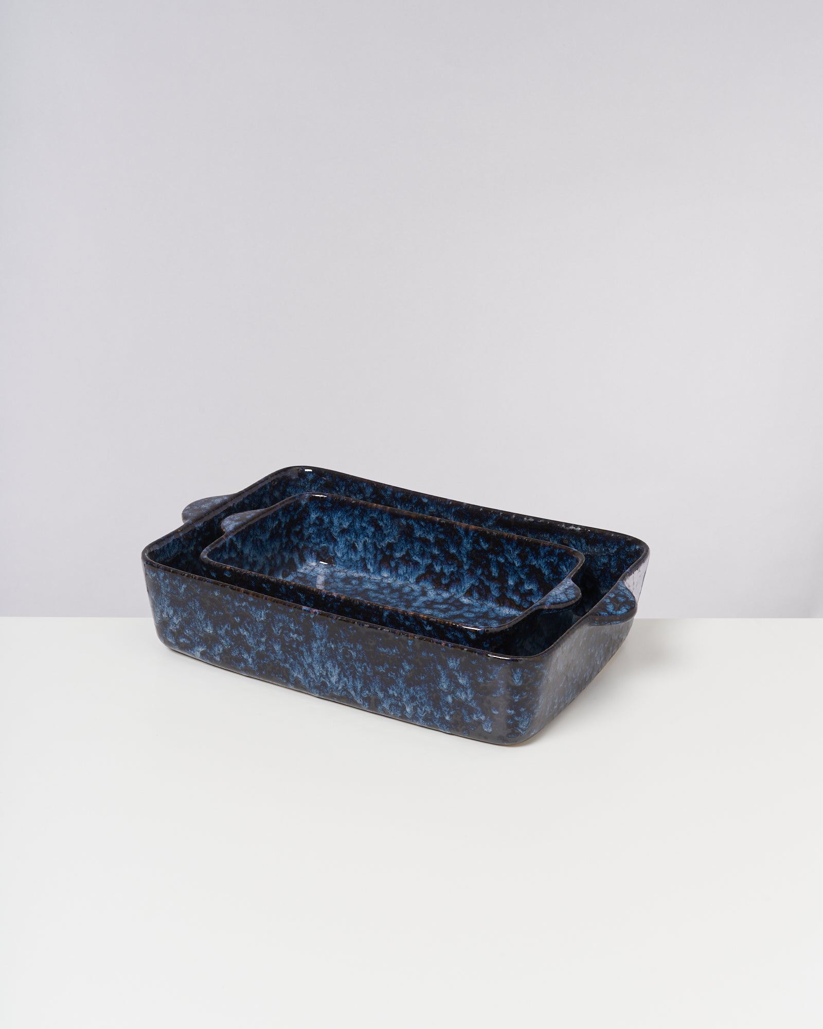 Zwei ineinander gestapelte, blau gesprenkelte Keramik-Auflaufformen auf einem weißen Hintergrund.