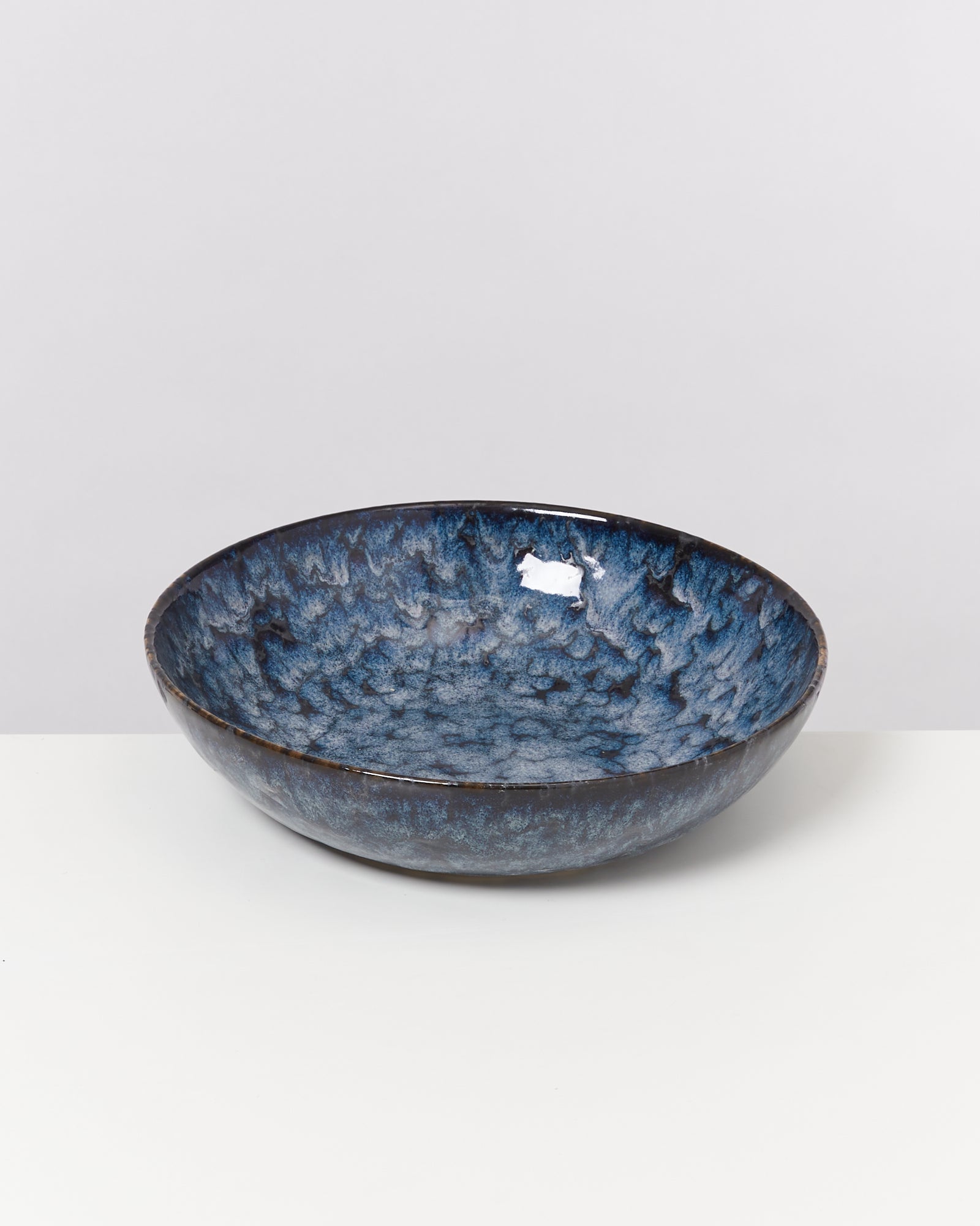 Blaue, glasierte Keramikschale mit gemustertem Innenbereich auf einem weißen Hintergrund.