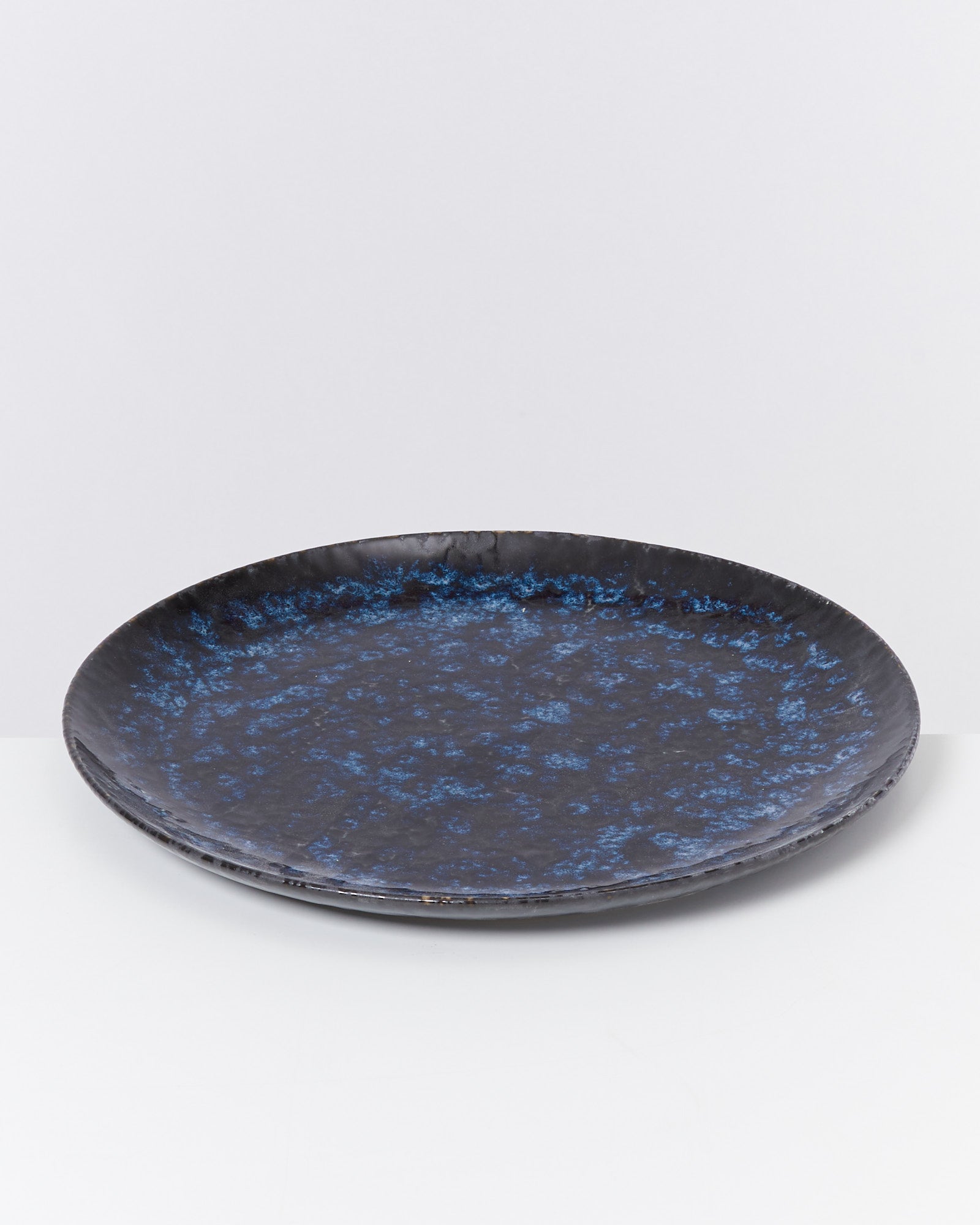 Dunkelblauer Teller mit marmoriertem Muster vor einem weißen Hintergrund.