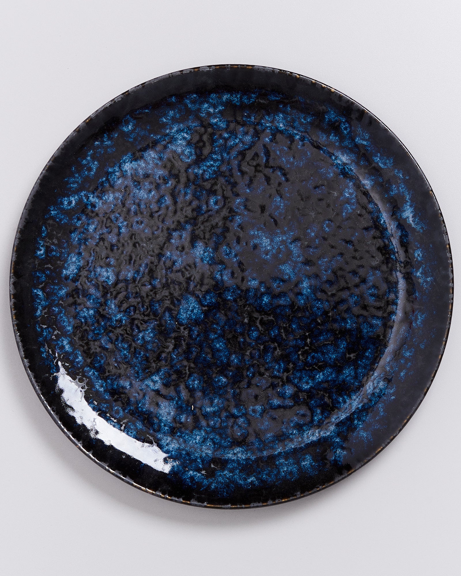 Runder Keramikteller mit blauer und schwarzer marmorierter Textur auf hellem Hintergrund.