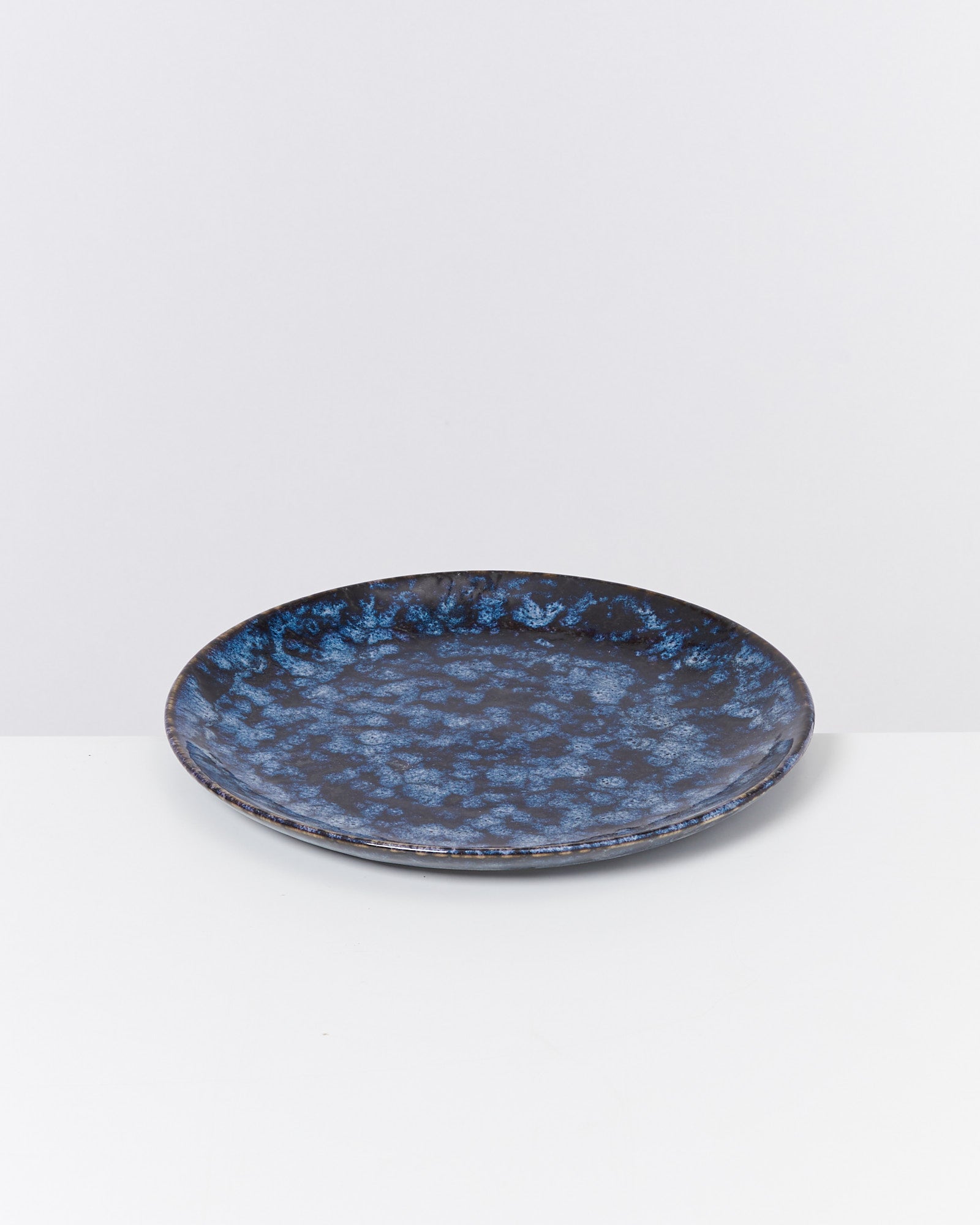 Schwarzer Teller mit blauer Marmorierung auf einem weißen Hintergrund.