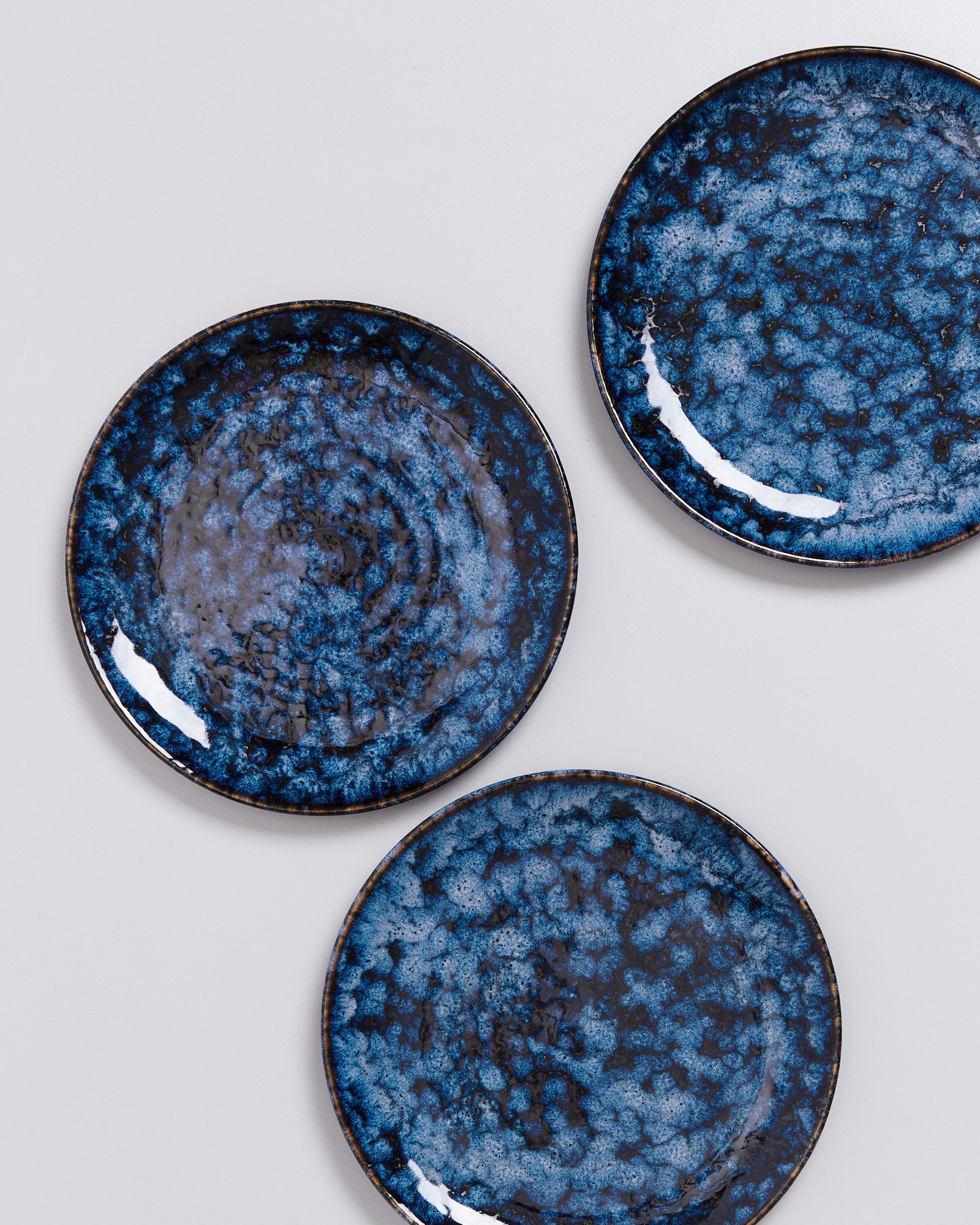 Drei dunkelblaue Keramikteller mit gesprenkeltem Muster auf einer grauen Oberfläche.