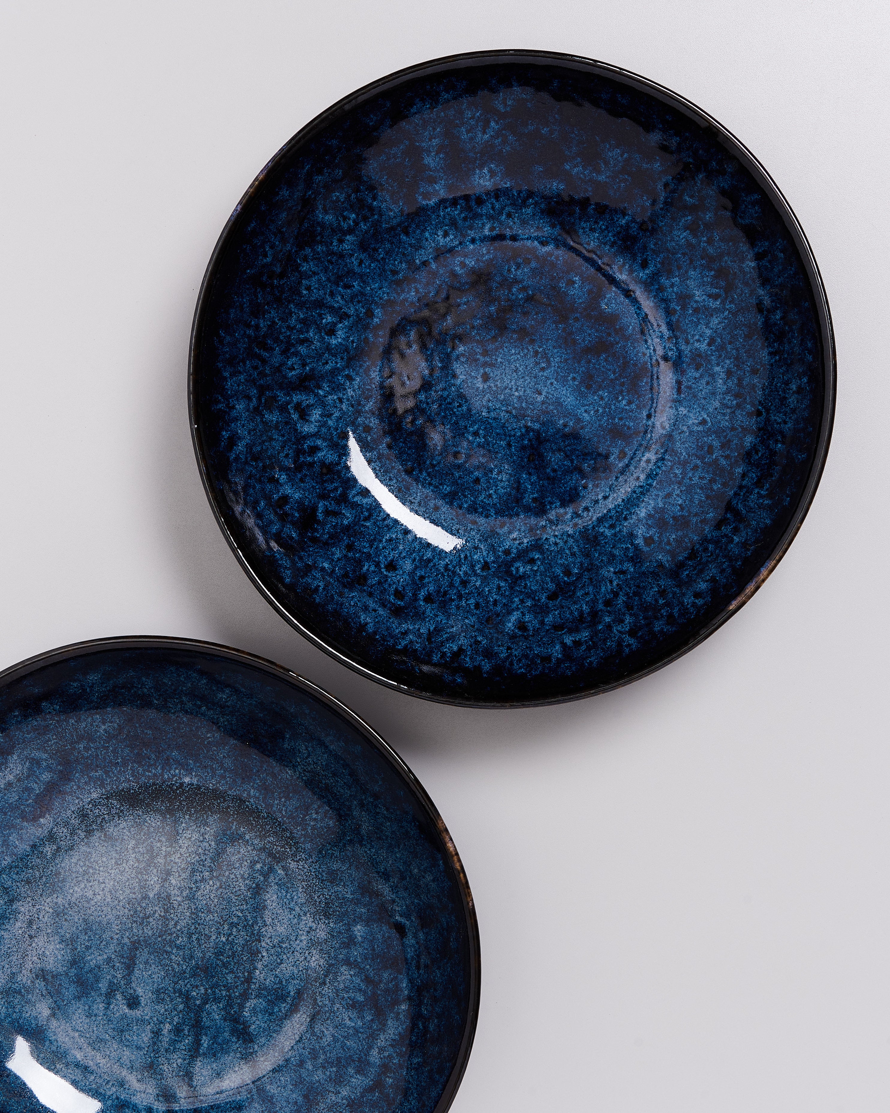 Zwei grob glasierte, dunkelblaue Keramikteller auf einem weißen Hintergrund.