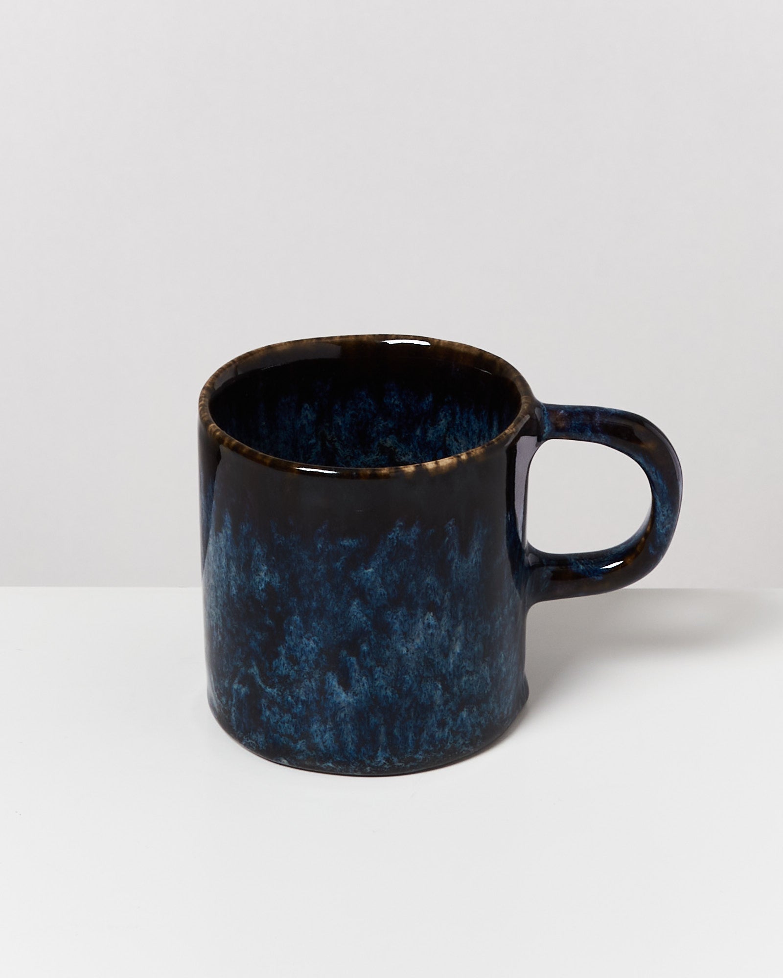 Dunkelblaue Keramiktasse mit künstlerischem Farbverlauf steht auf einem weißen Hintergrund.