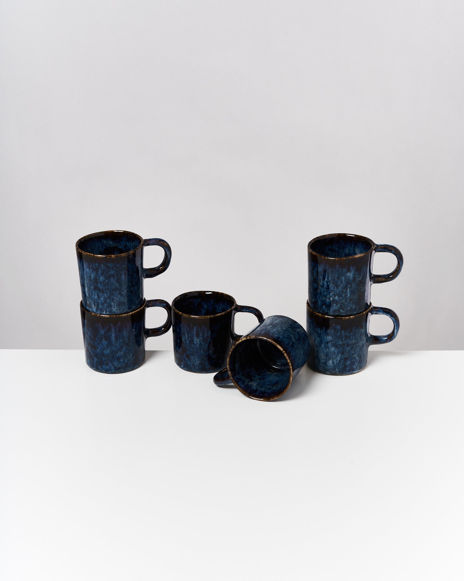 Sechs blau-schwarz marmorierte Tassen, zwei gestapelt, zwei seitlich liegend, auf weißem Hintergrund.
