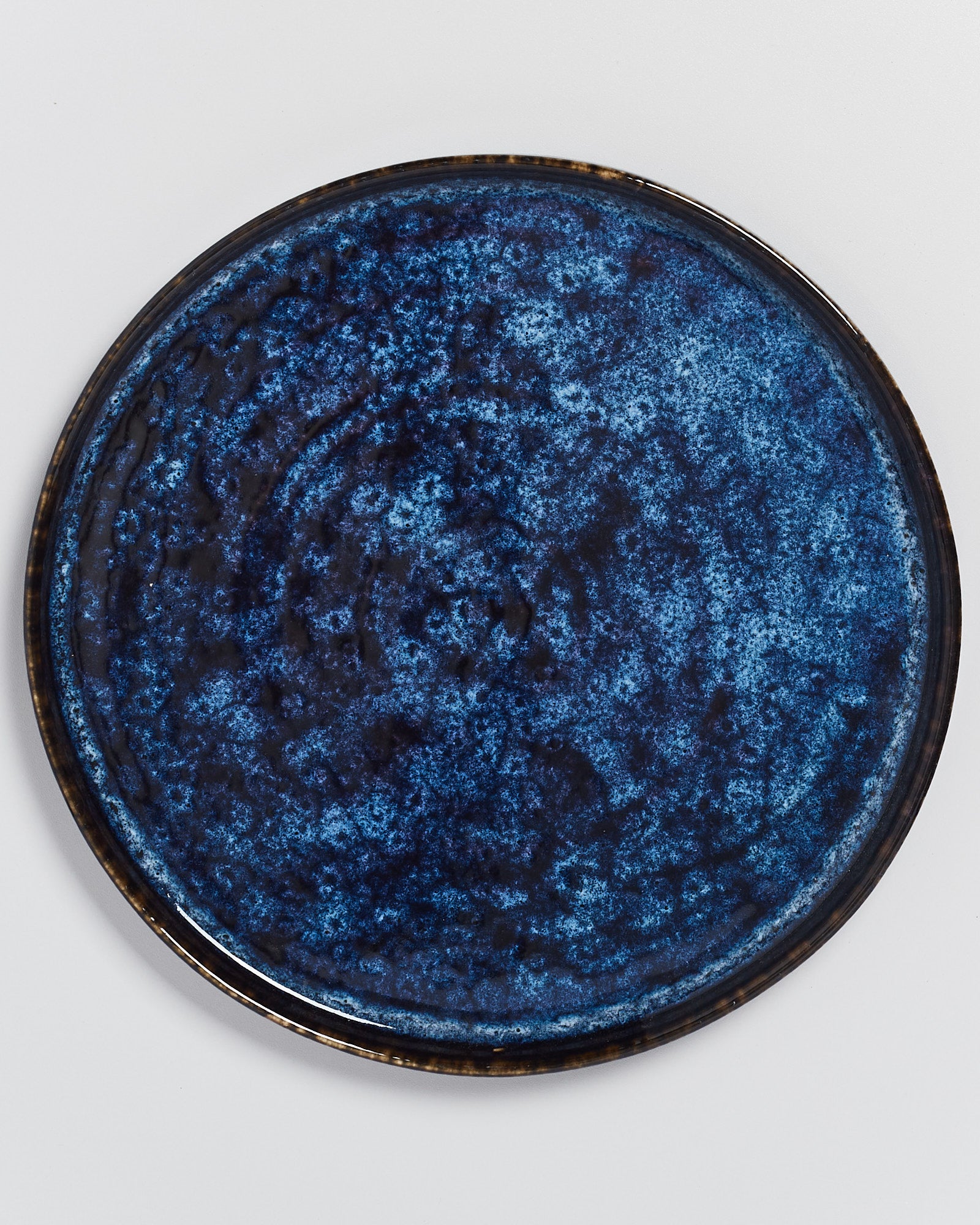 Runder Teller mit tiefblauer, gesprenkelter Glasur auf weißem Hintergrund.
