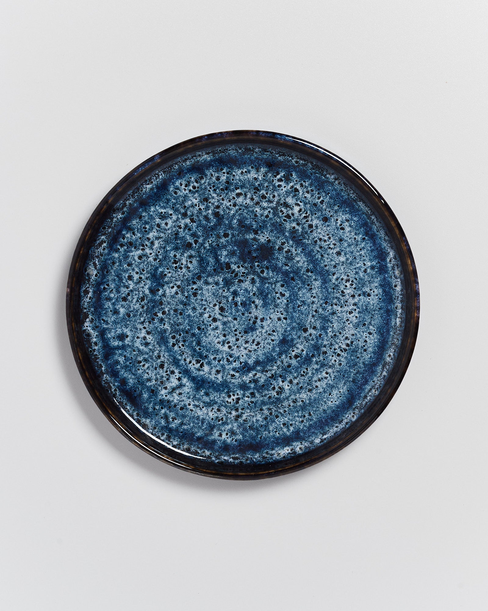 Ein runder, blau gesprenkelter Keramikteller auf weißem Hintergrund.